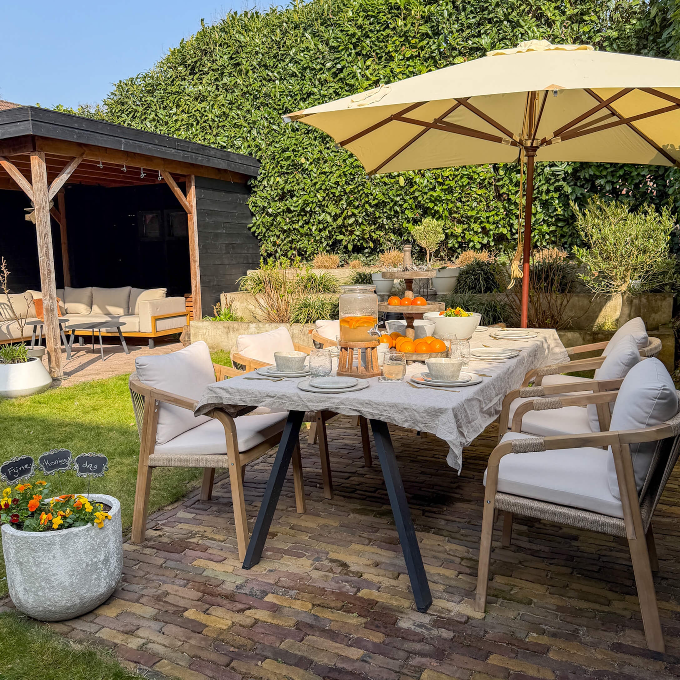 Tuinmeubelset met houten stoelen en beige parasol op stenen terras met sinaasappeldecoratie