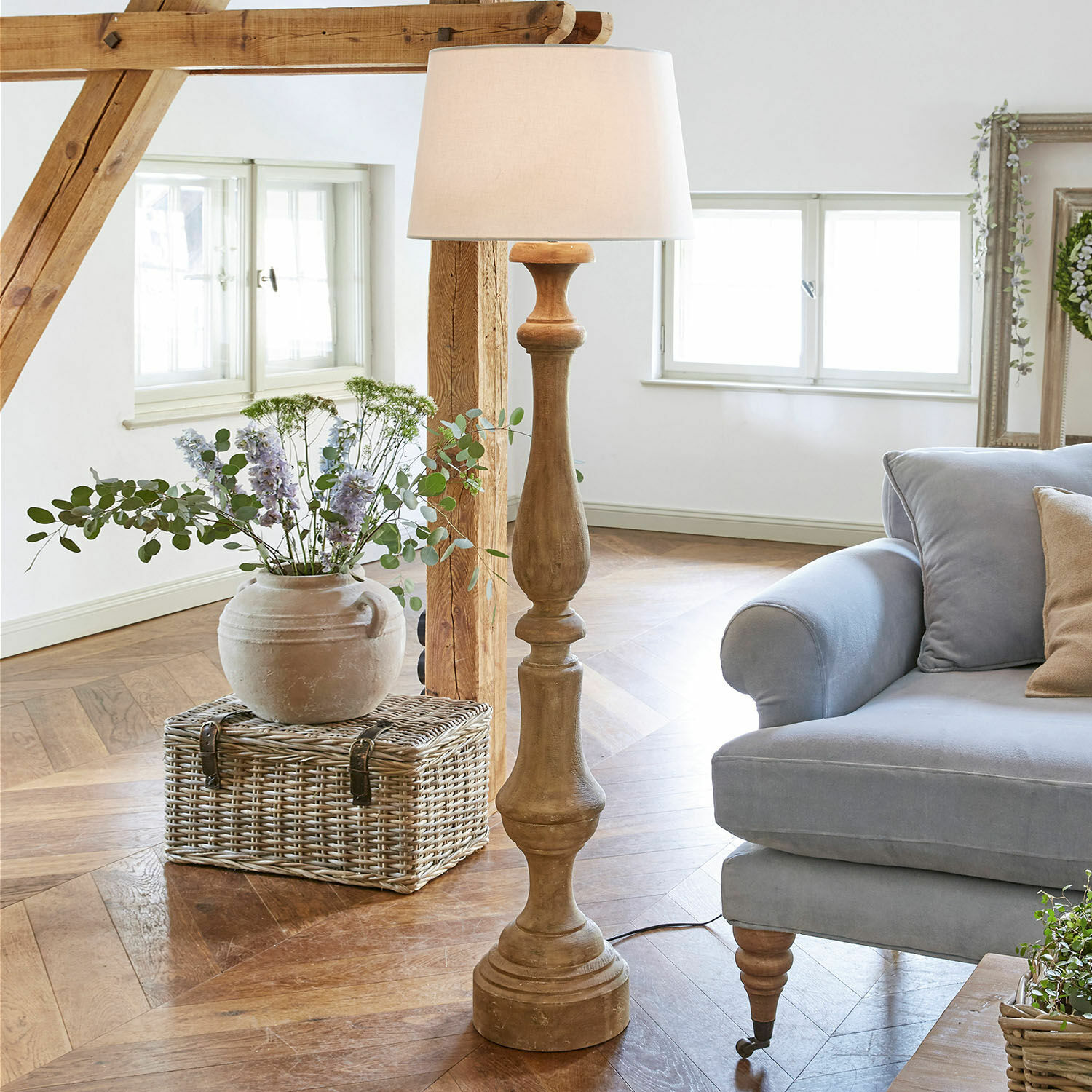 Staande lamp Etienne Houten vloerlamp met witte kap in lichte woonkamer met blauwe bank en rieten mand