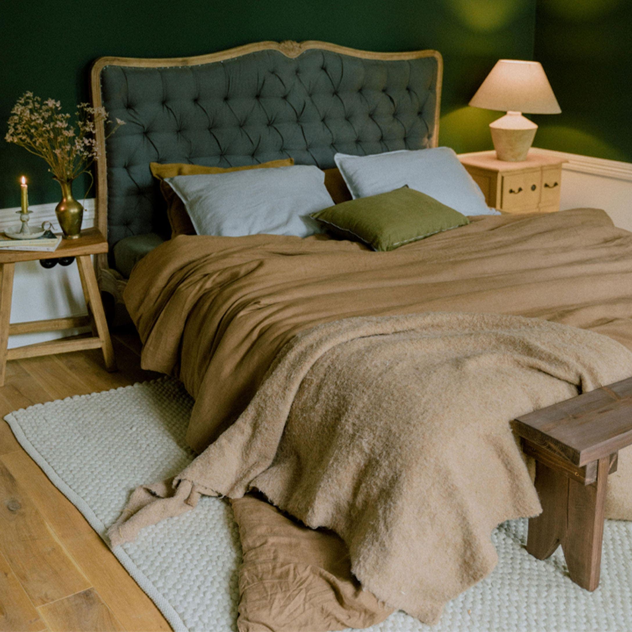 Gezellig bed met groen gestoffeerd hoofdeinde en bruin beddengoed in slaapkamer
