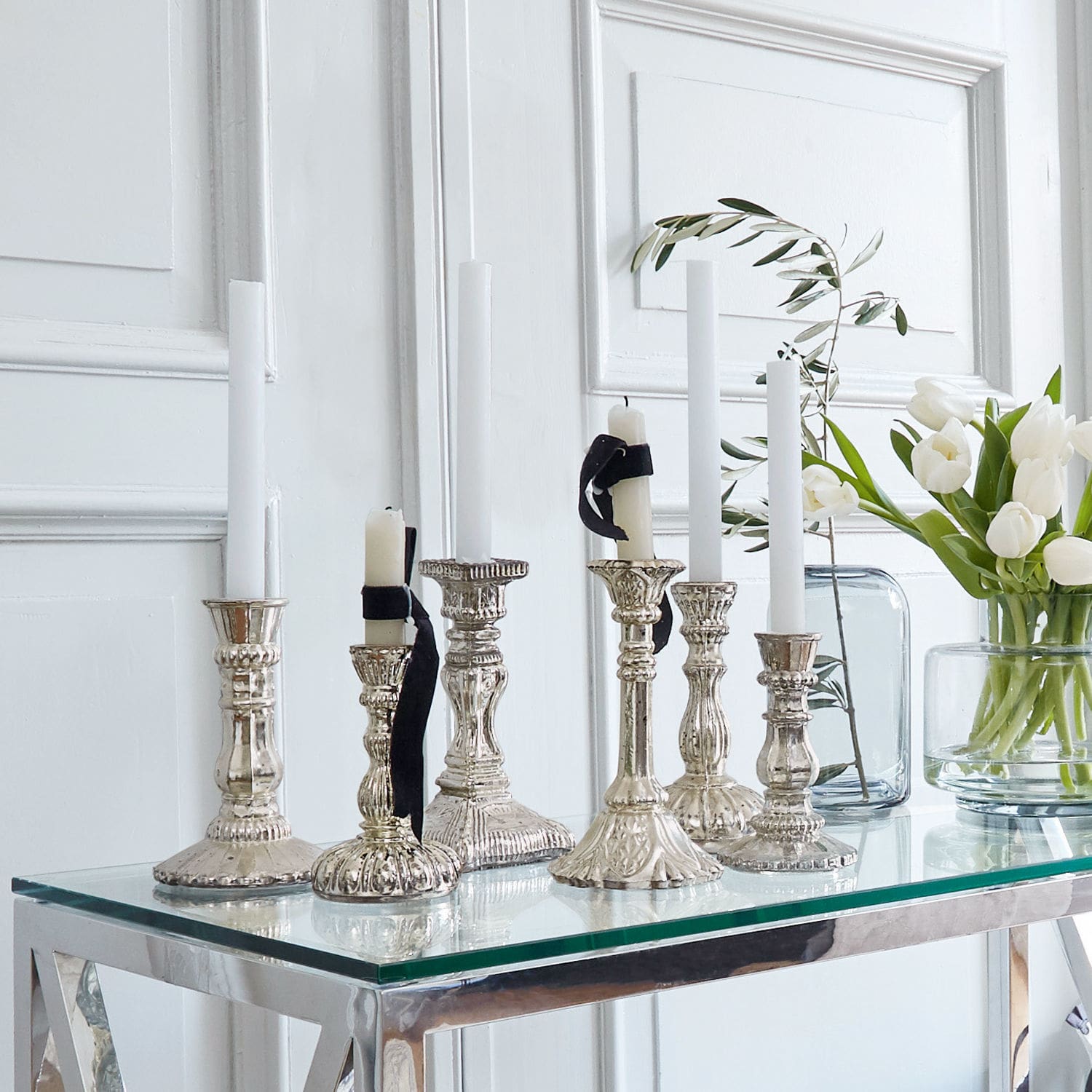 Kandelaar set van 6 Adolpha Set zilverkleurige metalen kandelaars met witte kaarsen op glazen tafel in lichte kamer