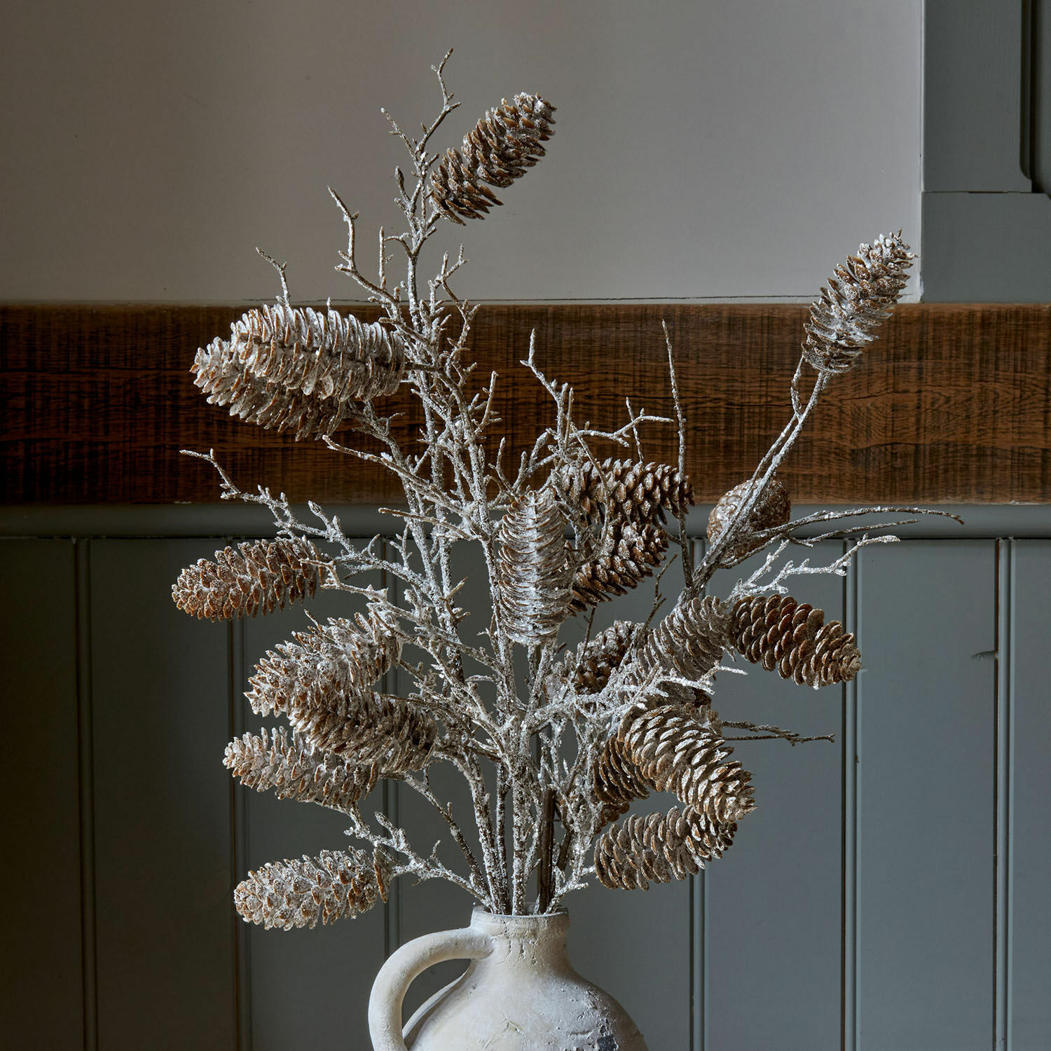 Decoratieve takken met dennenappels in witte vaas tegen houten achtergrond, natuurlijke interieurdecoratie