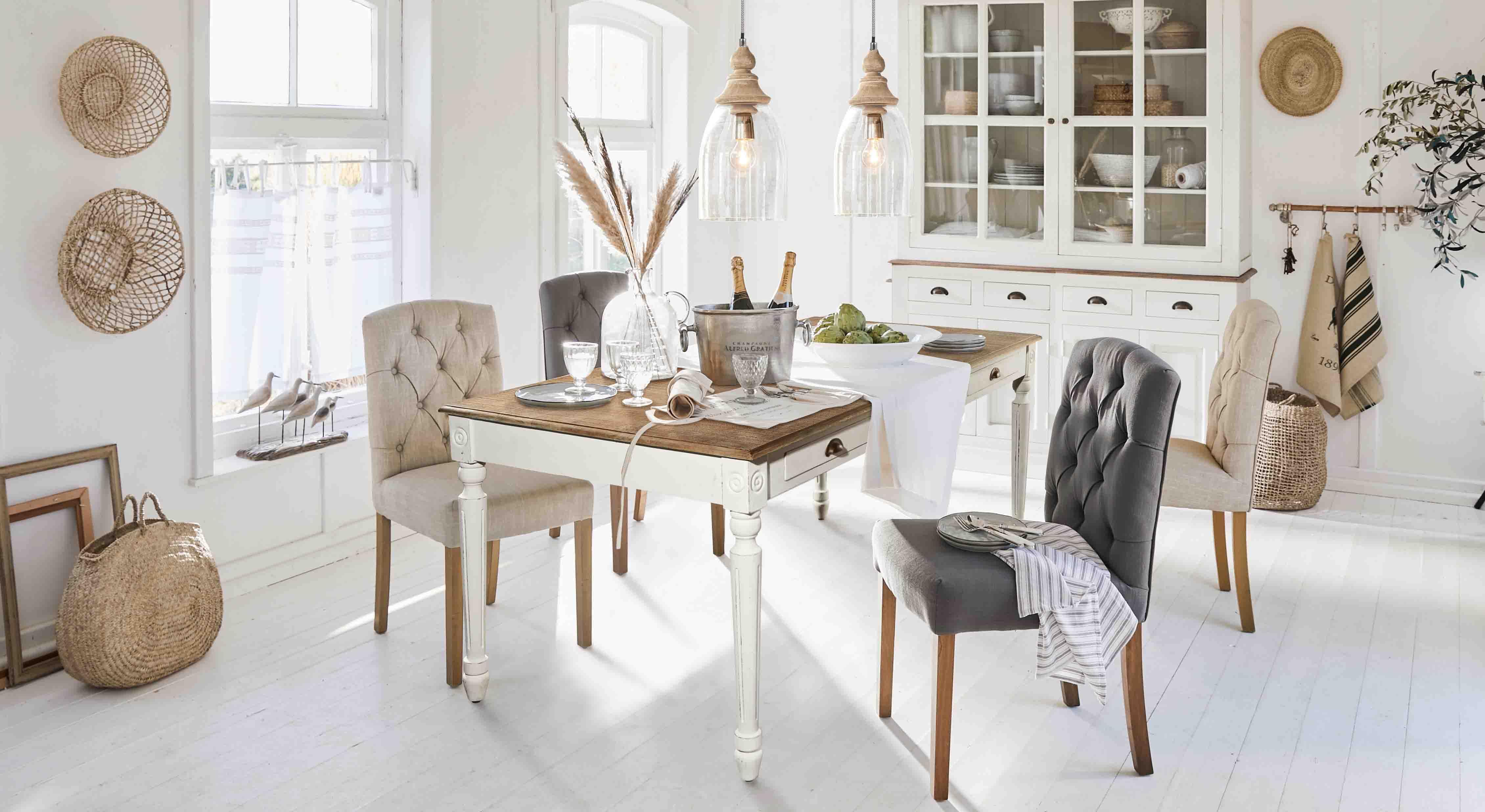 Rustieke eetkamer met witte houten tafel en gestoffeerde stoelen in beige en grijs in een lichte ruimte