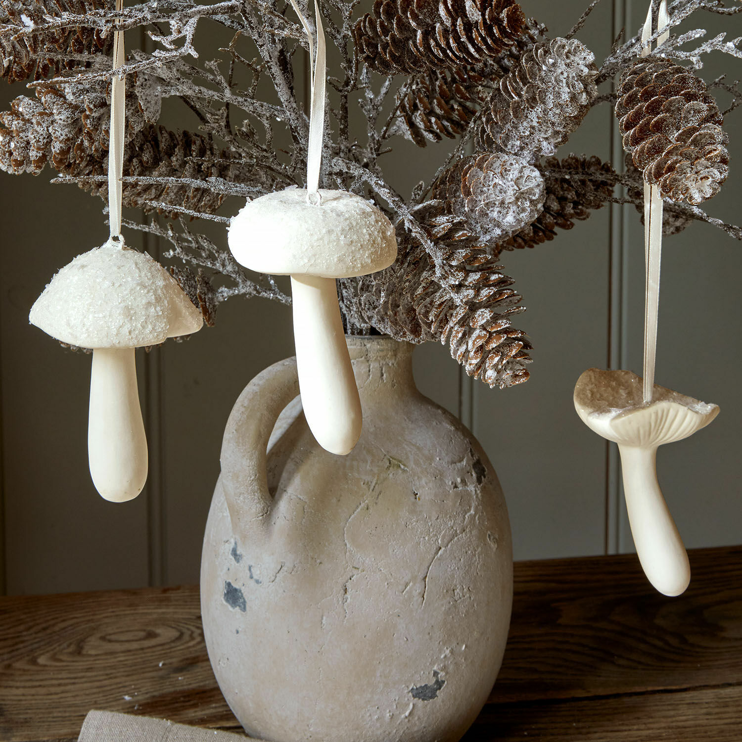 Sierpaddenstoel set van 3 Qilexor Witte decoratieve paddenstoelenhangers aan takken met dennenappels in een aardewerken vaas op houten tafel
