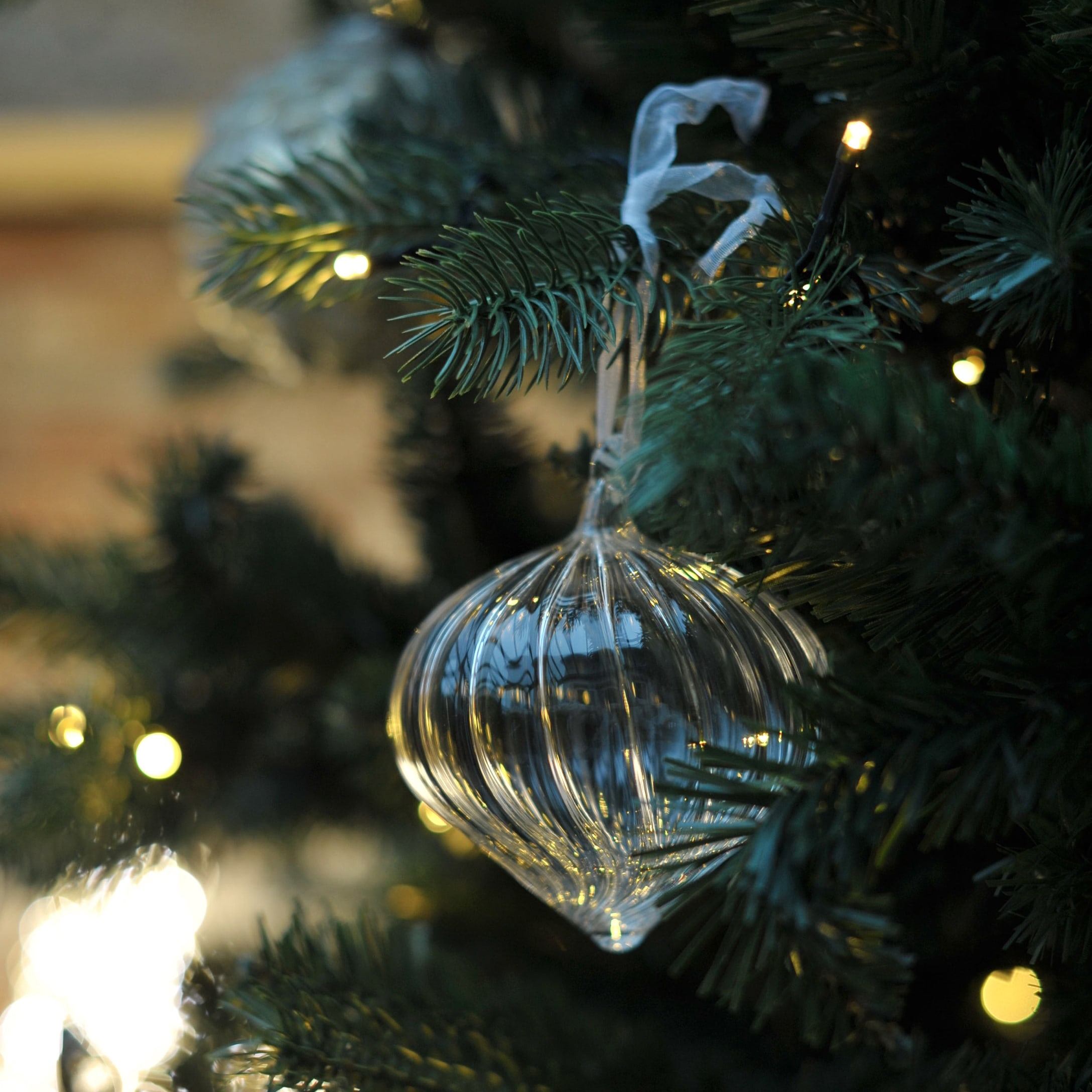 Transparante glazen kerstbal in ui-vorm aan groene tak met kerstverlichting