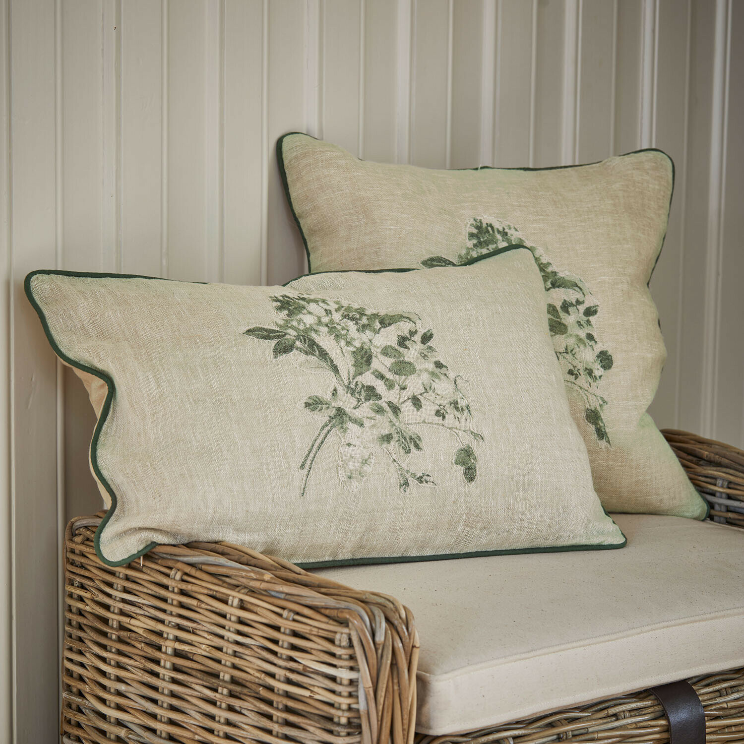 Beige linnen kussens met groene plantenprint en groene bies op rotan bank