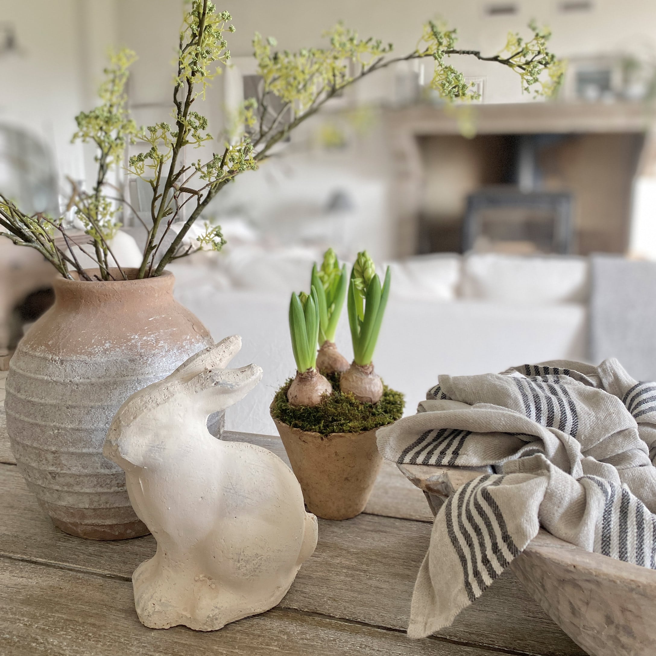 Decoratief wit keramisch konijn naast pot met groene scheuten en linnen doek op houten tafel