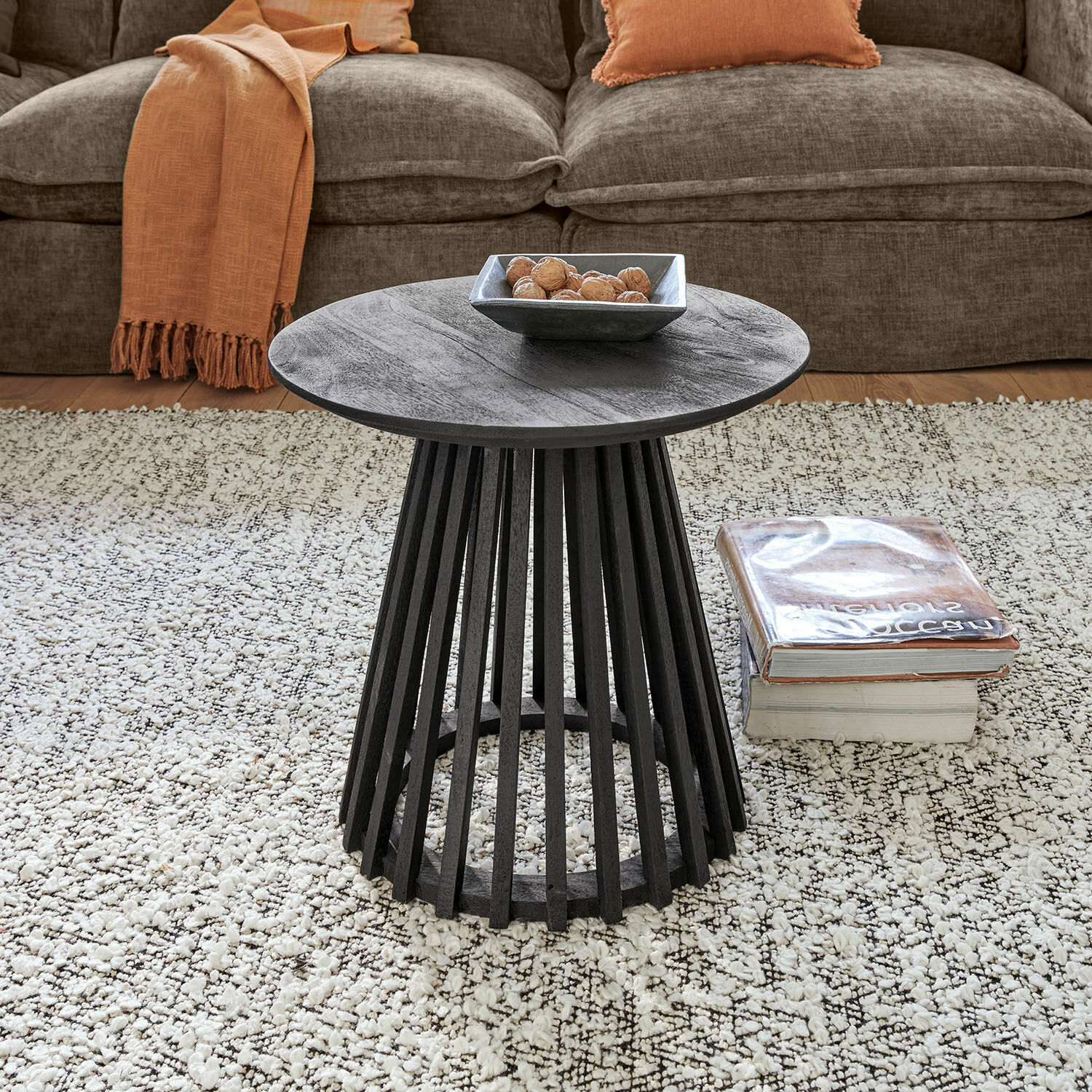 Ronde zwarte houten salontafel met open onderstel op lichte vloerkleed in woonkamer