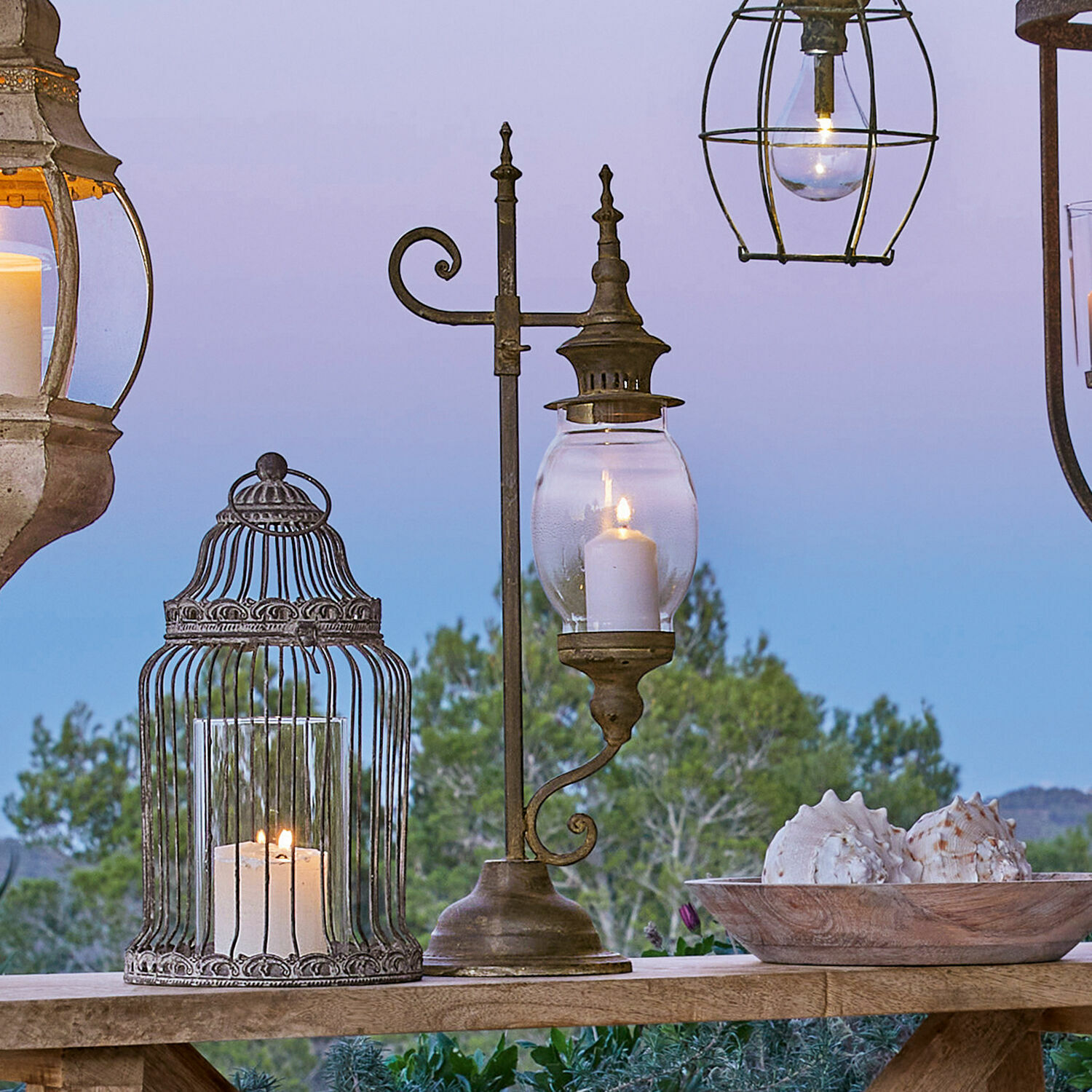 Metalen lantaarn met helder glas en brandende kaars op houten tafel met schelpendecoratie buiten