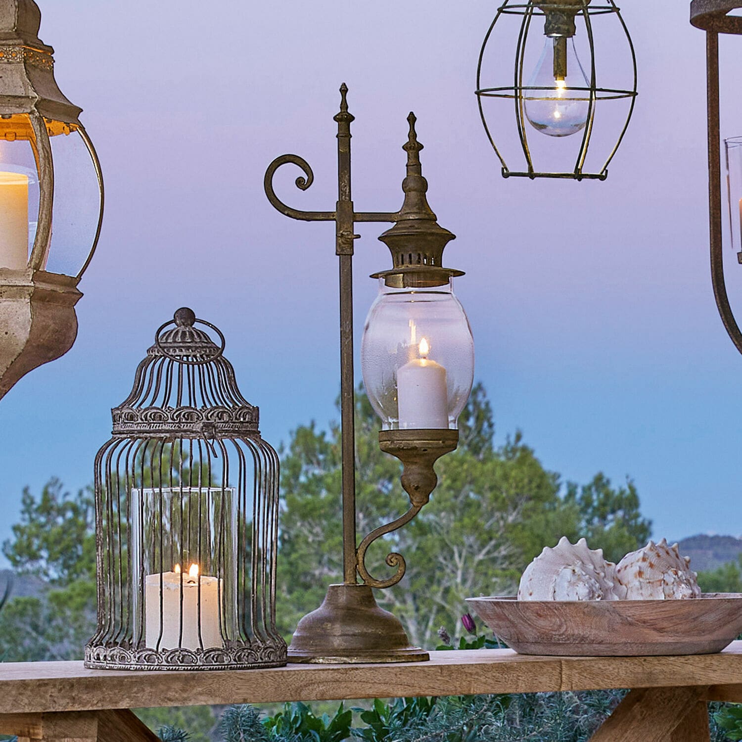 Lantaarn Bowral Metalen lantaarn met helder glas en brandende kaars op houten tafel met schelpendecoratie buiten