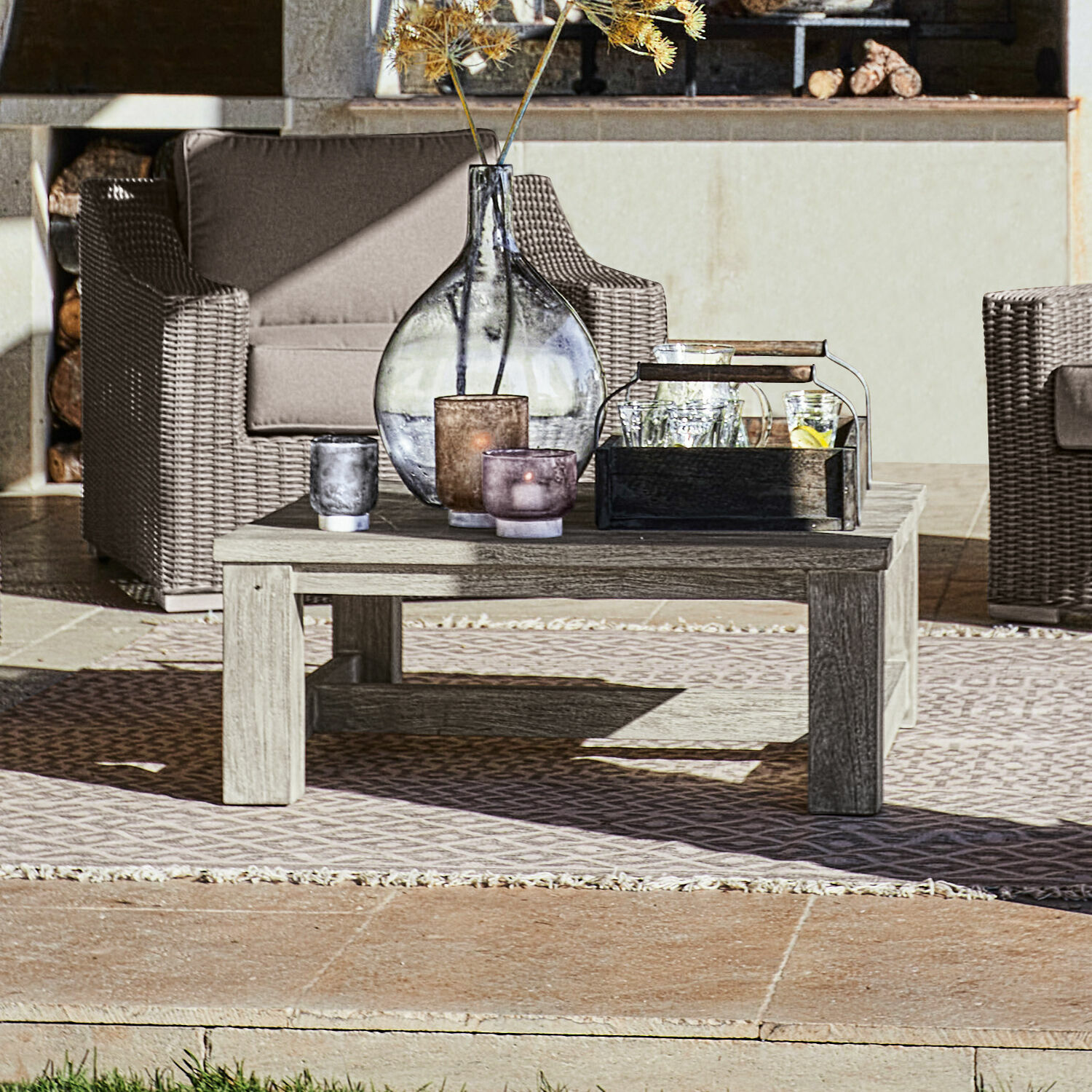 Salontafel Malden Lage houten salontafel op terras met decoratieve kaarsen en vaas, rotan tuinmeubilair op de achtergrond