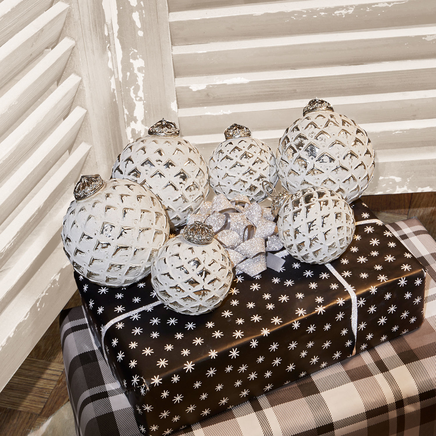 Witte kerstballen met ruitpatroon op zwart-wit ingepakte cadeaus in rustieke omgeving