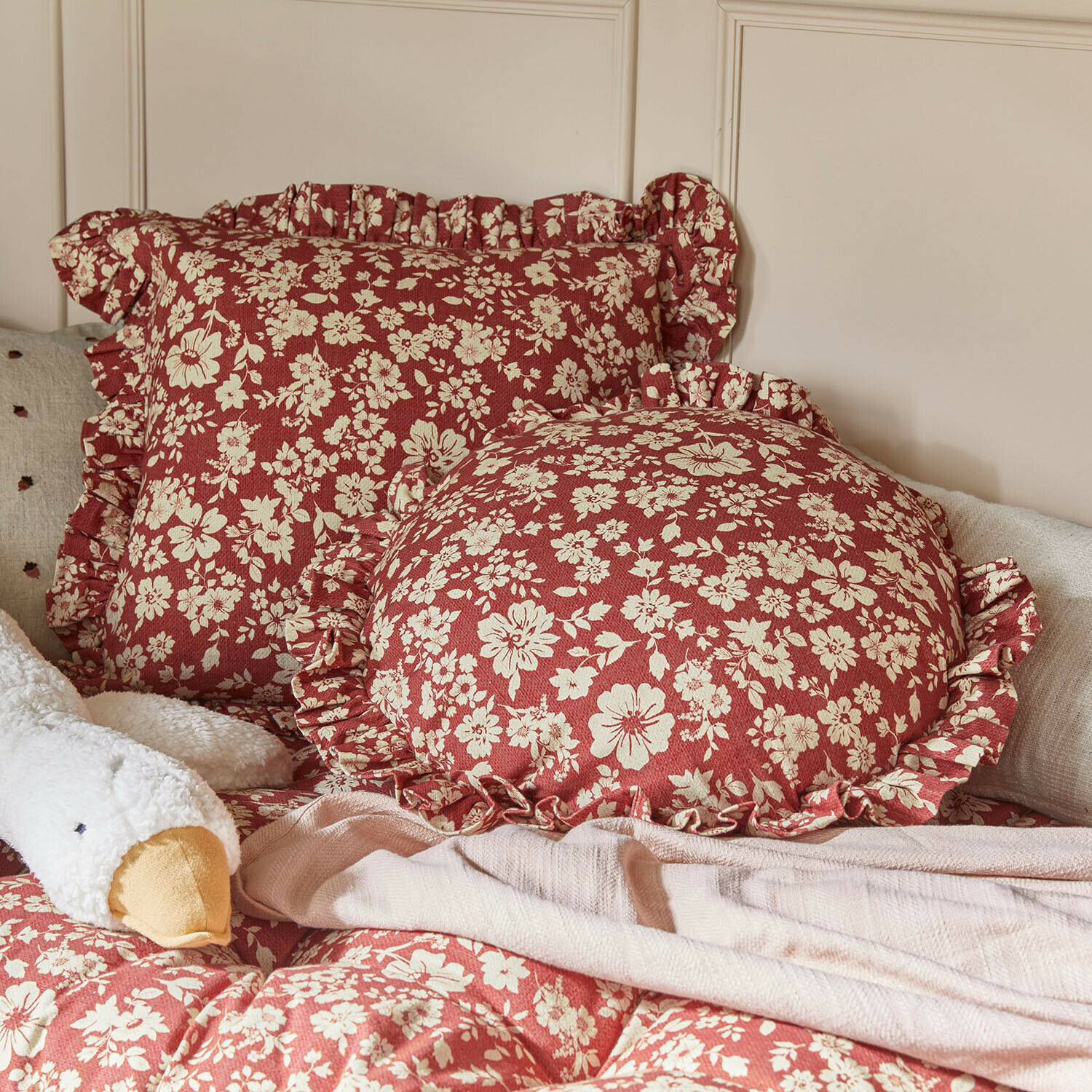 Kussen set van 2 Frambelle Rode sierkussens met crème bloemenpatroon en ruches op bed met zachte deken
