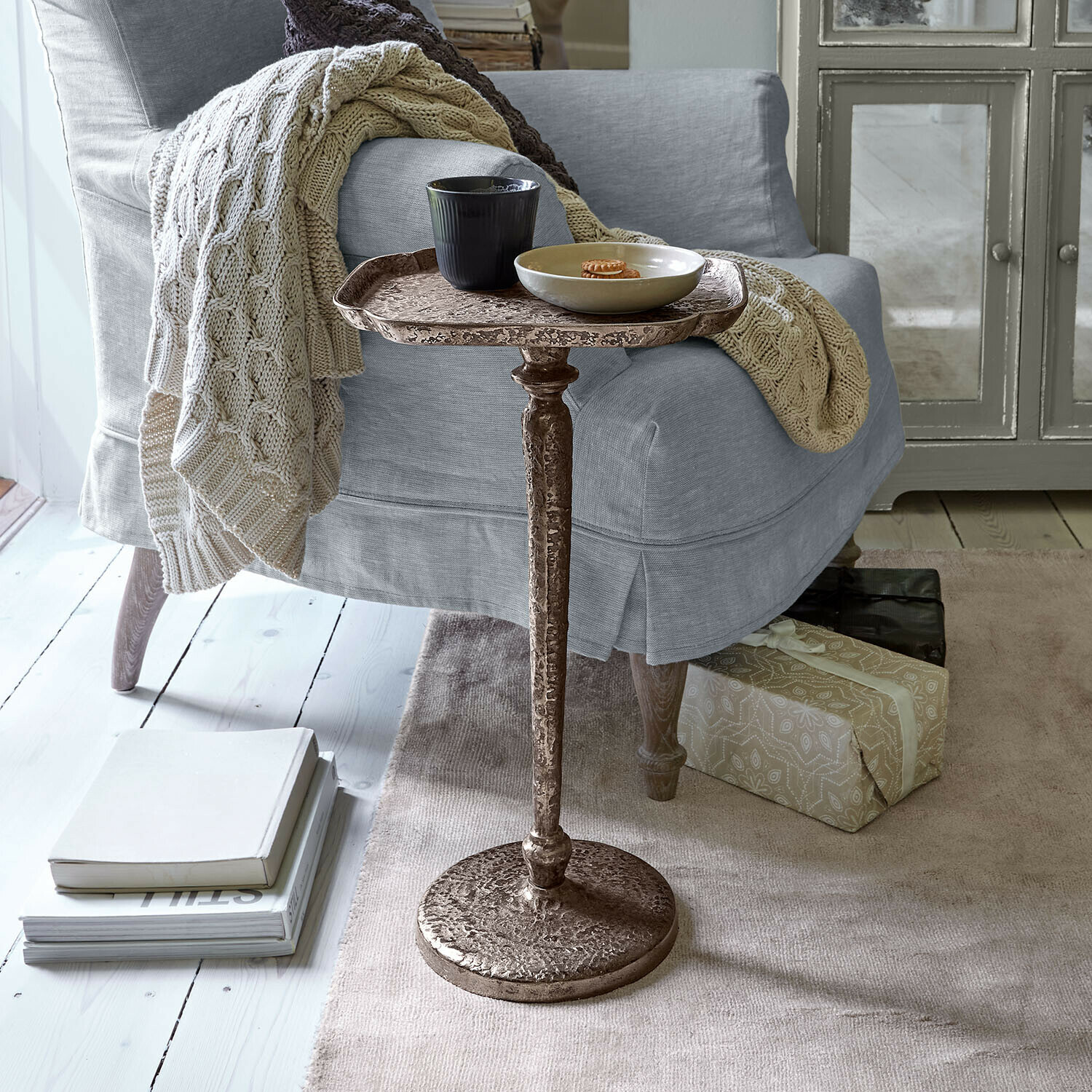 Bruine metalen bijzettafel naast een grijze fauteuil met gebreide deken en boeken