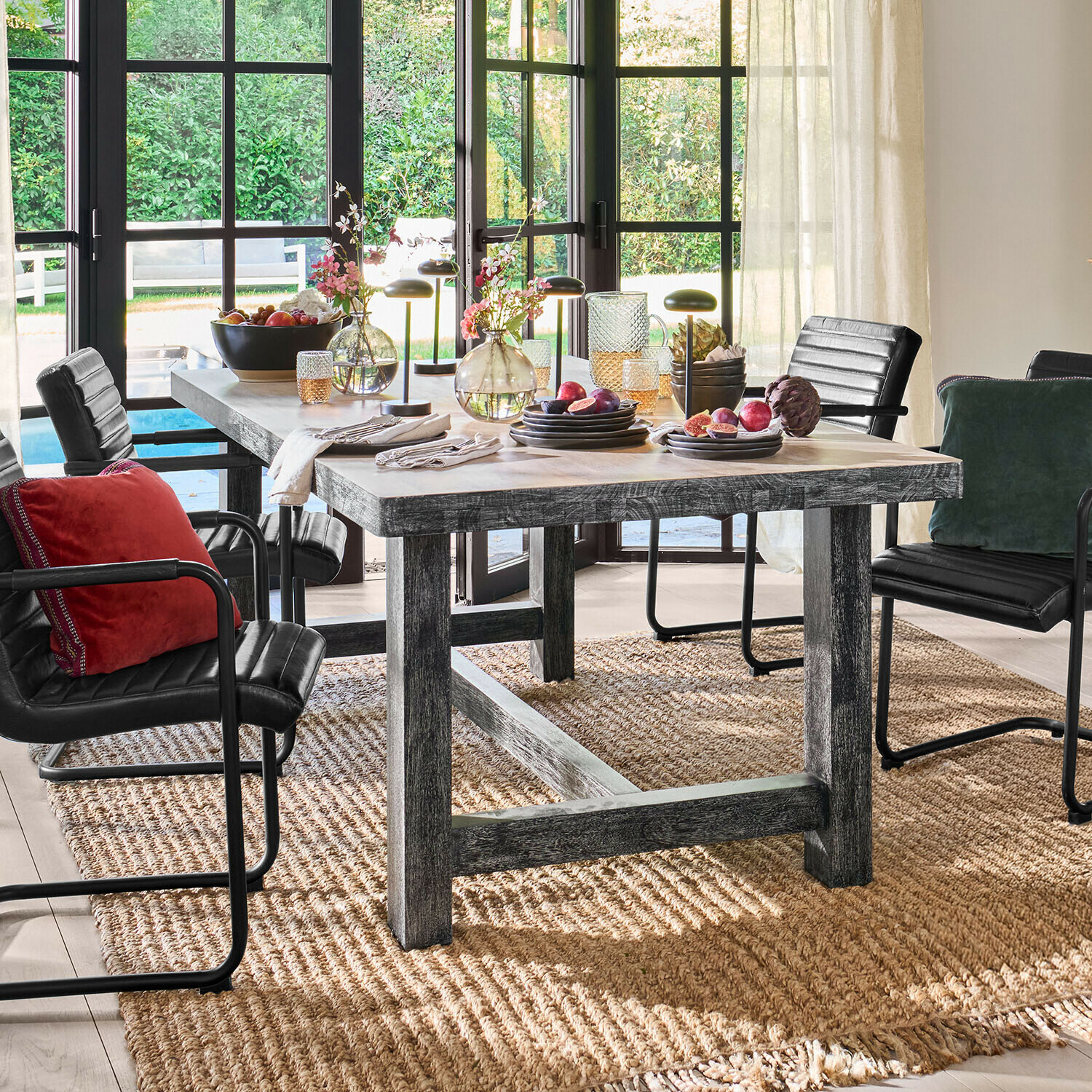 Rustieke houten eettafel met zwarte stoelen en decoraties op natuurlijke vloerkleed in lichte kamer