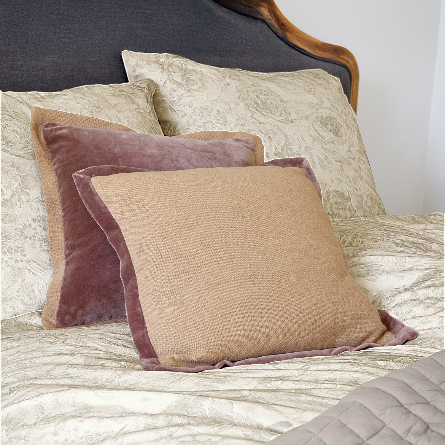 Beige en roze sierkussens van fluweel en stof op bed met lichte beddengoed
