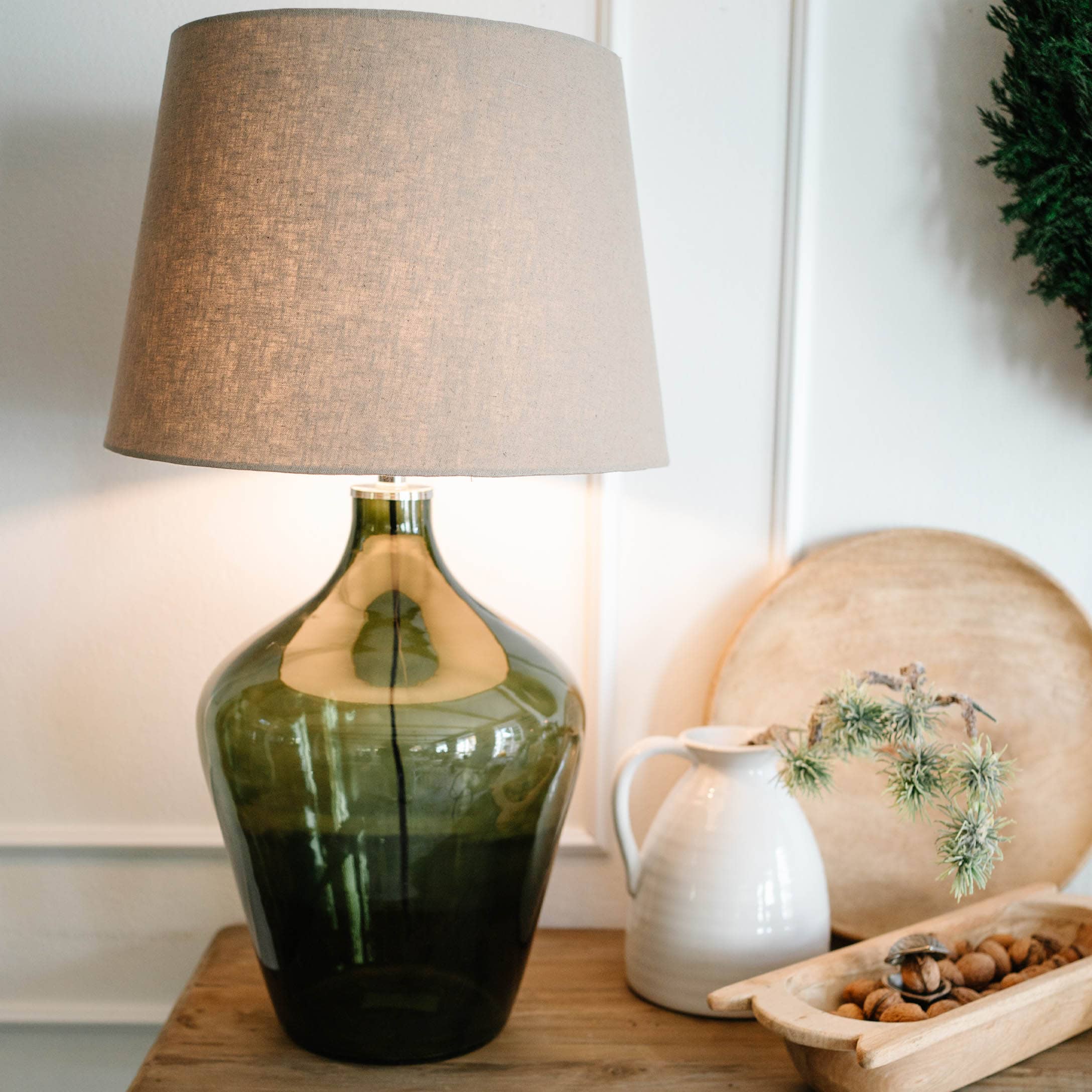 Tafellamp van groen glas met beige kap op houten tafel met decoraties