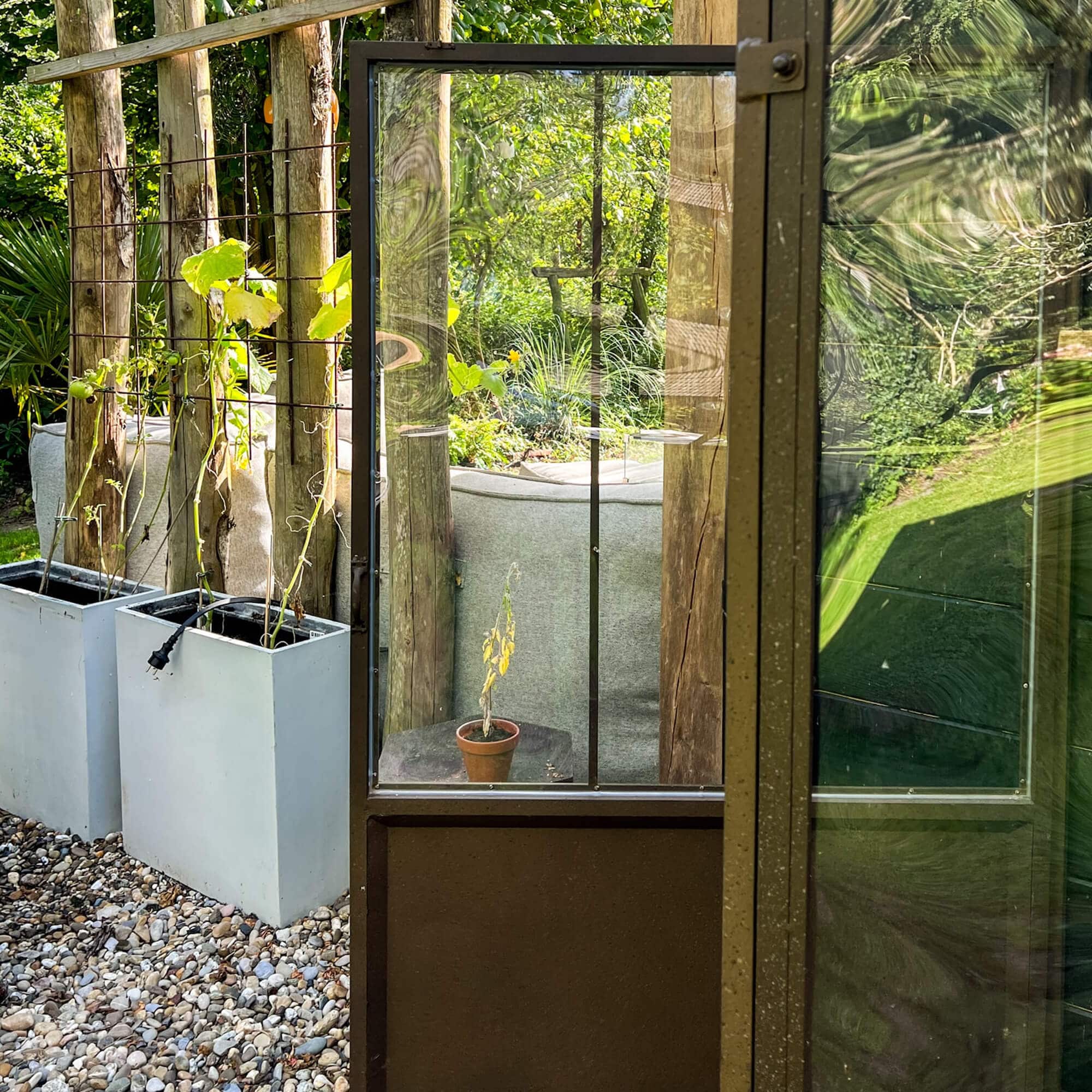 Tuin deur met glas en metalen frame voor plantenbakken en groene tuin