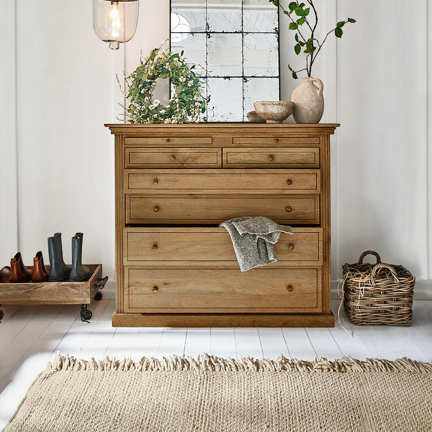 Houten ladekast in natuurlijke kleur met meerdere lades, decoraties en lichte vloerkleed in lichte kamer