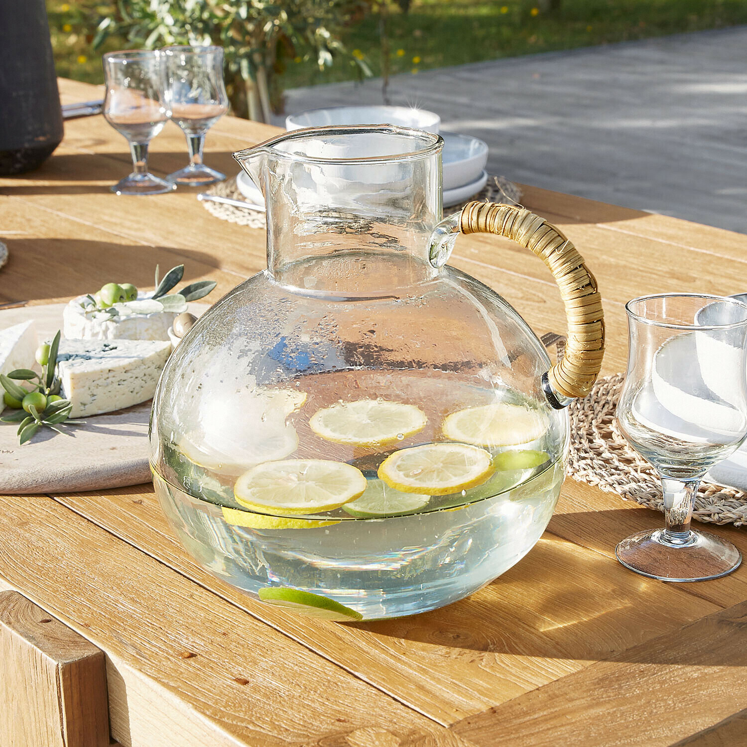 Glazen karaf met rotan handvat op houten tafel, gevuld met water en schijfjes citroen en limoen