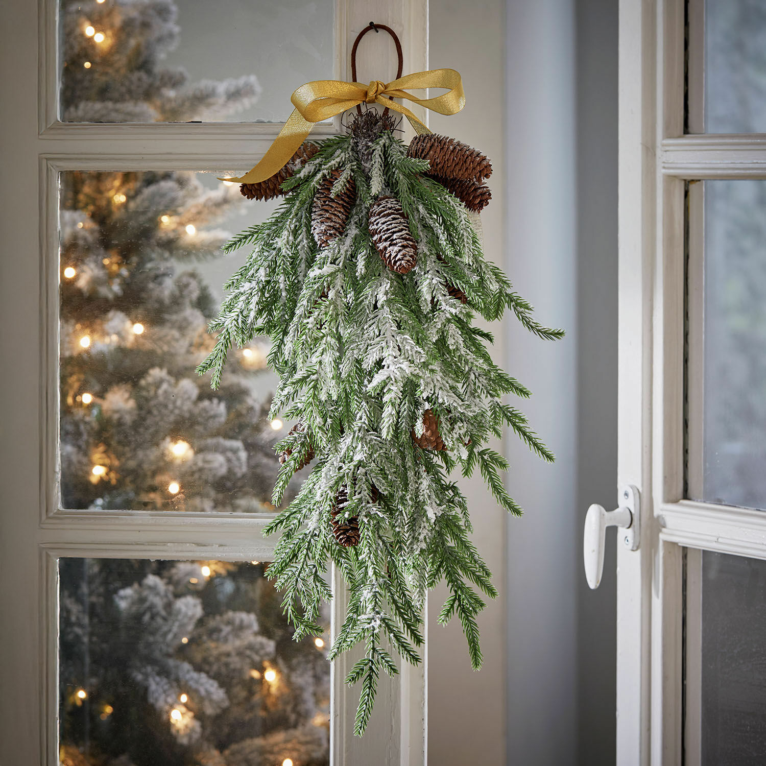 Kerstdecoratie van groene takken met dennenappels en nepsneeuw, versierd met gouden strik