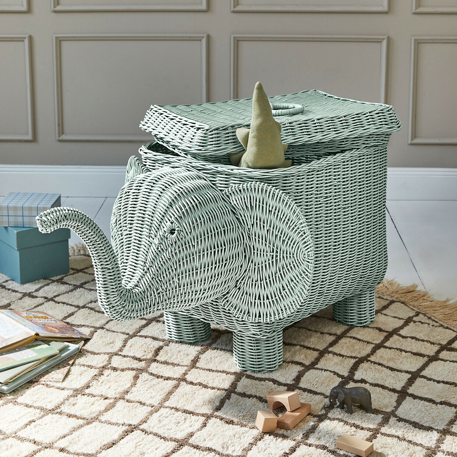 Mintgroene rieten mand in olifantvorm met open deksel en speelgoed op tapijt