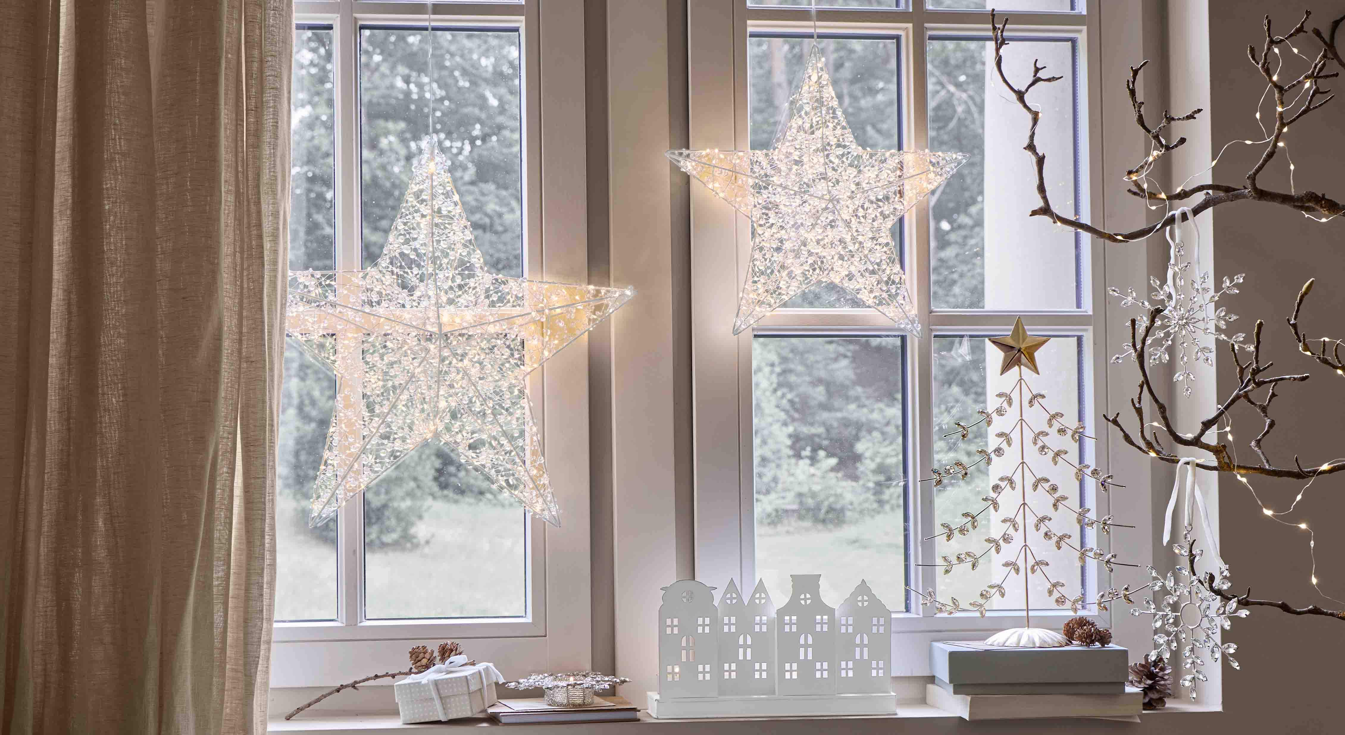 Decoratieve verlichte sterren van transparant materiaal hangend aan het raam, feestelijke binnenverlichting