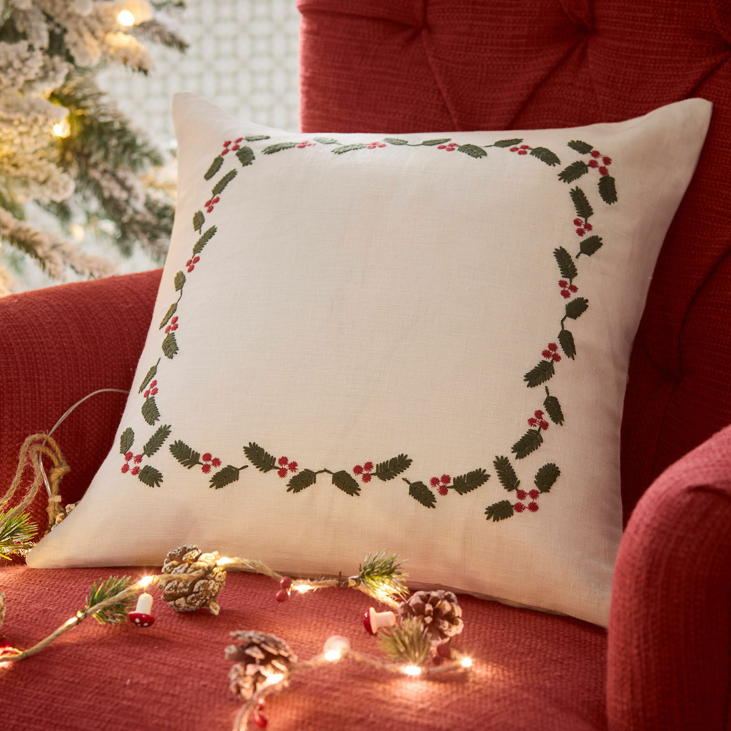 Witte linnen kussen met groene bladeren en rode bessen op rode stoel, kerstdecoratie