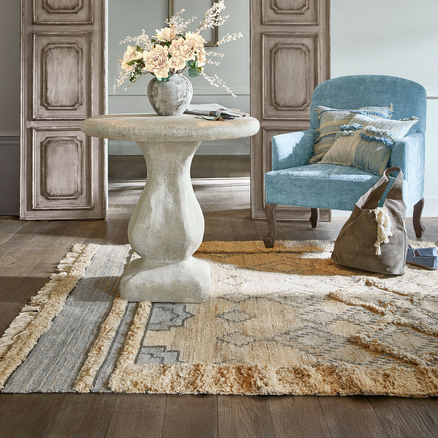 Ronde grijze betonnen tafel met vaas en bloemen op beige vloerkleed in stijlvolle woonkamer