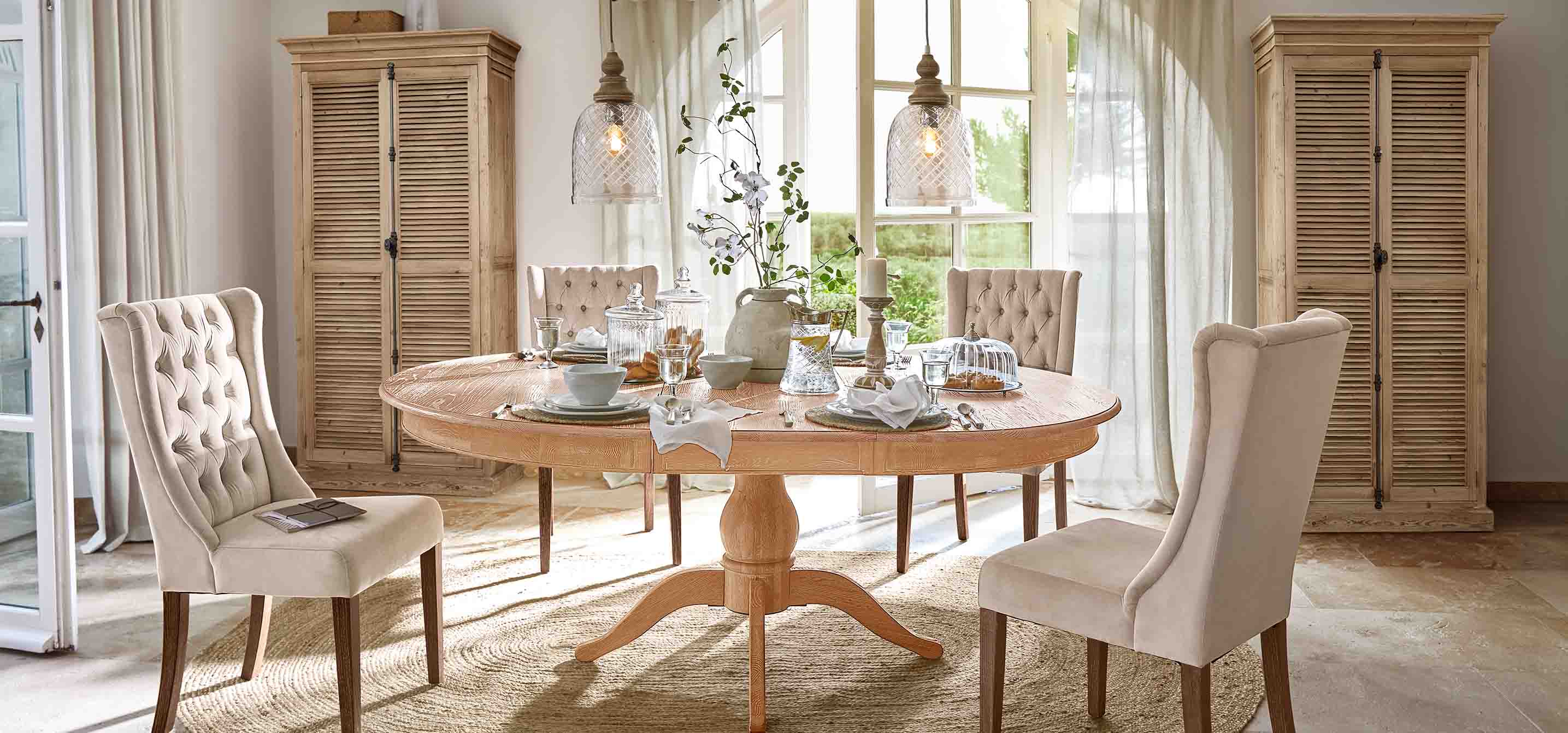 Eetkamer met ronde tafel van licht hout en beige gestoffeerde stoelen in vintage stijl