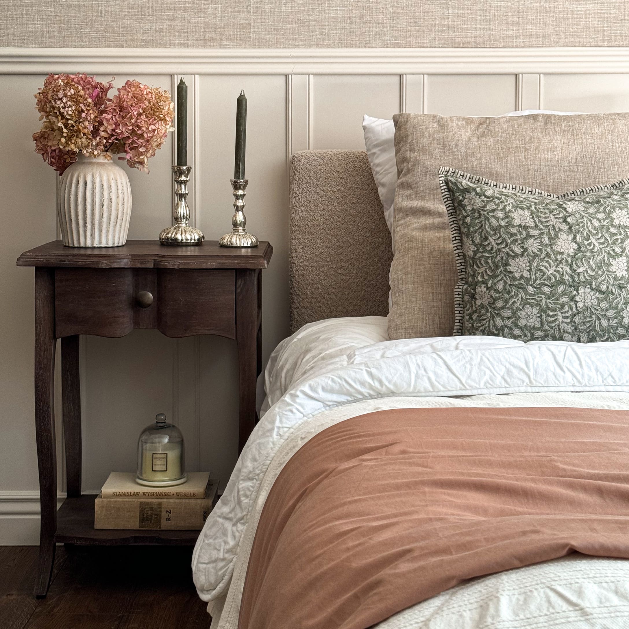 Gezellige slaapkamer met beige beddengoed, groen kussen en houten nachtkastje met decoraties