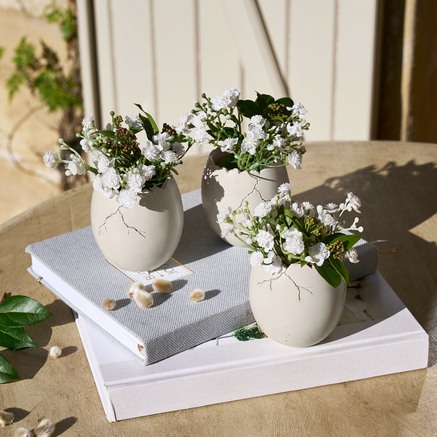 Decoratief ei set van 3 Waverlye Drie witte keramische vazen in eivorm met witte bloemen op houten tafel met boeken