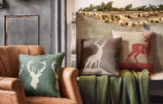 Decoratieve kussens met hertenmotief in natuurlijke kleuren op leren stoel en bank met groene deken