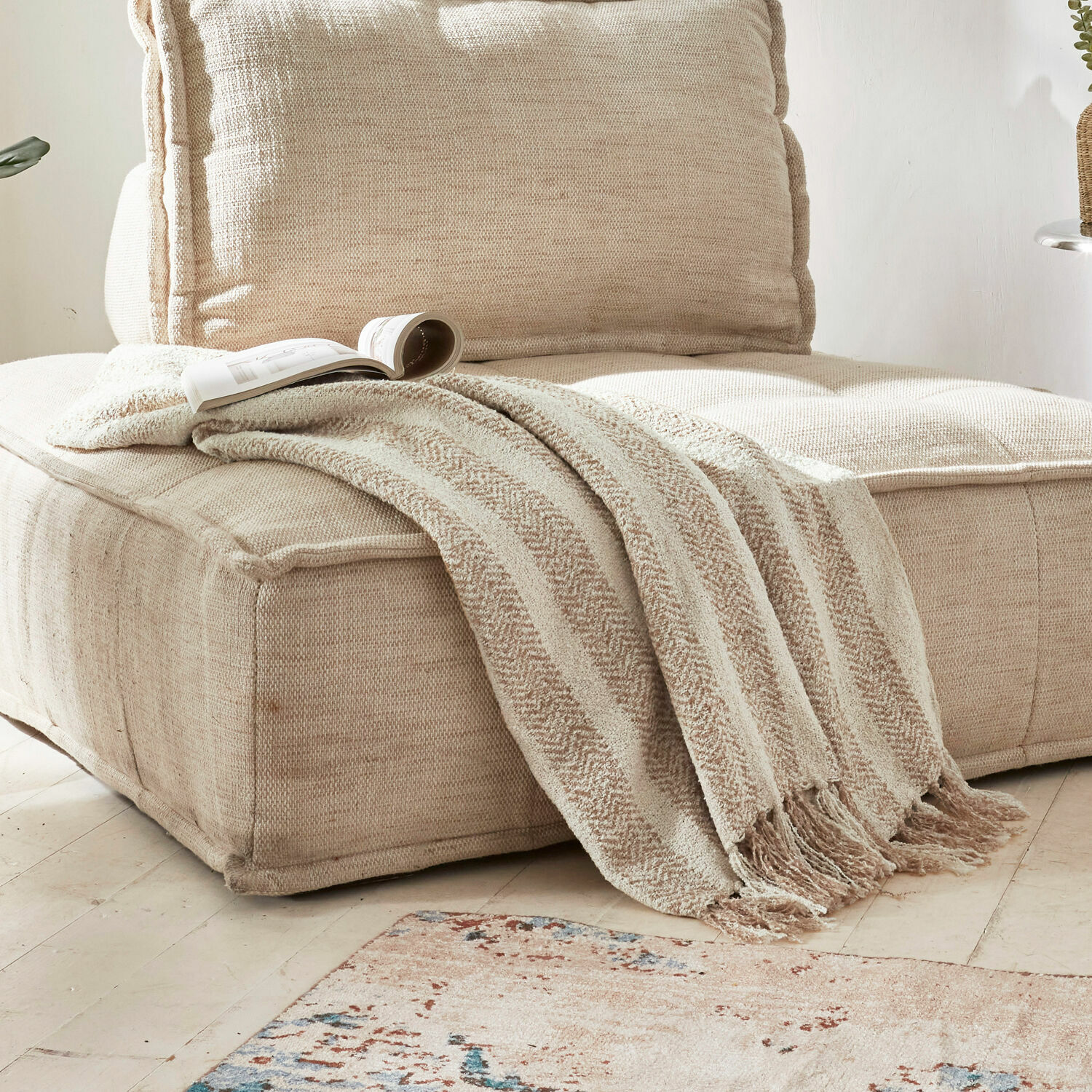 Beige zachte deken met franjes op beige stoffen bank in lichte woonkamer