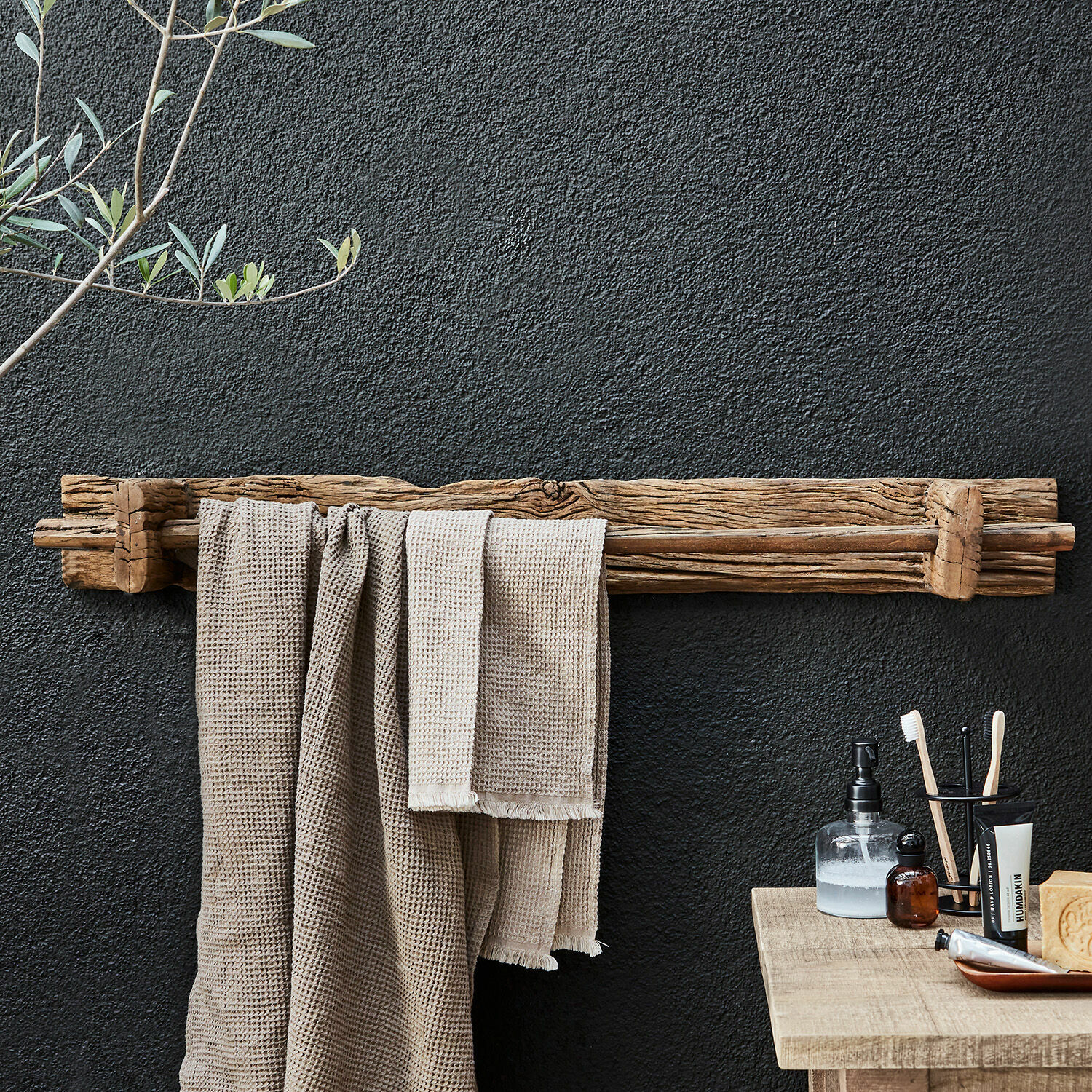Rustieke houten handdoekhouder in natuurlijke kleur aan zwarte muur in badkamer