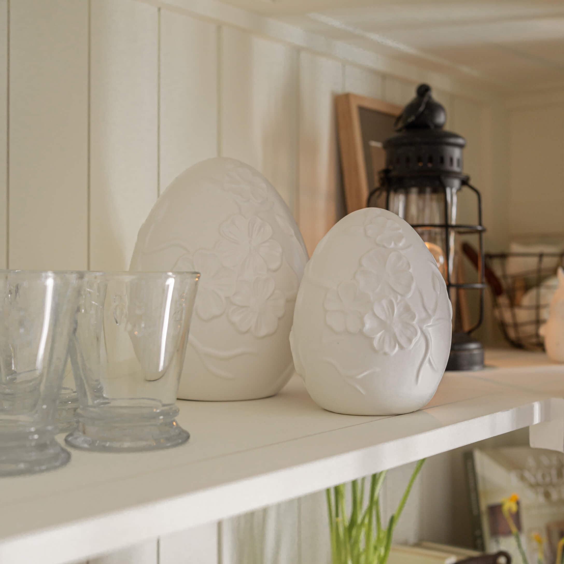 Witte albasten eivormige decoraties met bloemmotief op rustiek plankje geplaatst