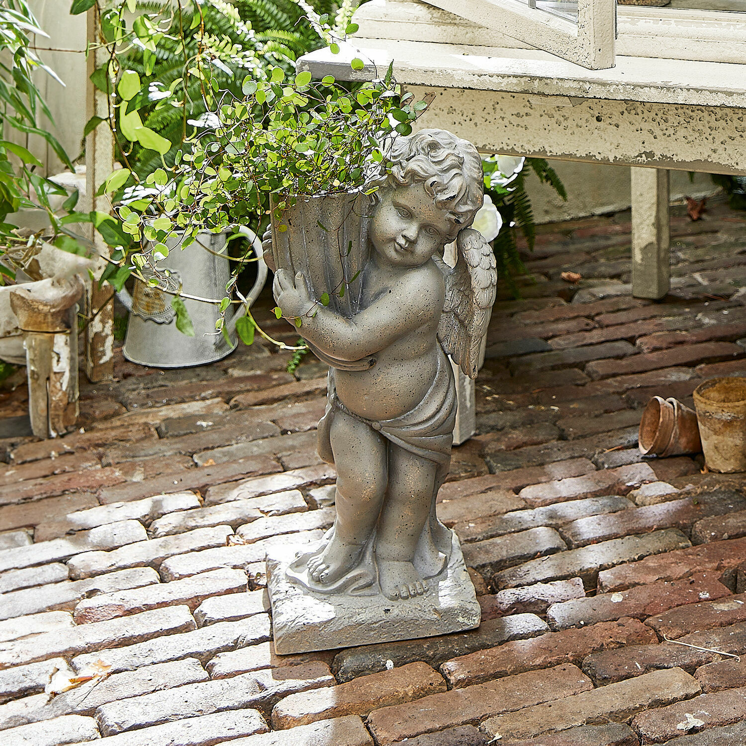 Grijs stenen engelbeeld met bloempot en groene plant op een bakstenen vloer