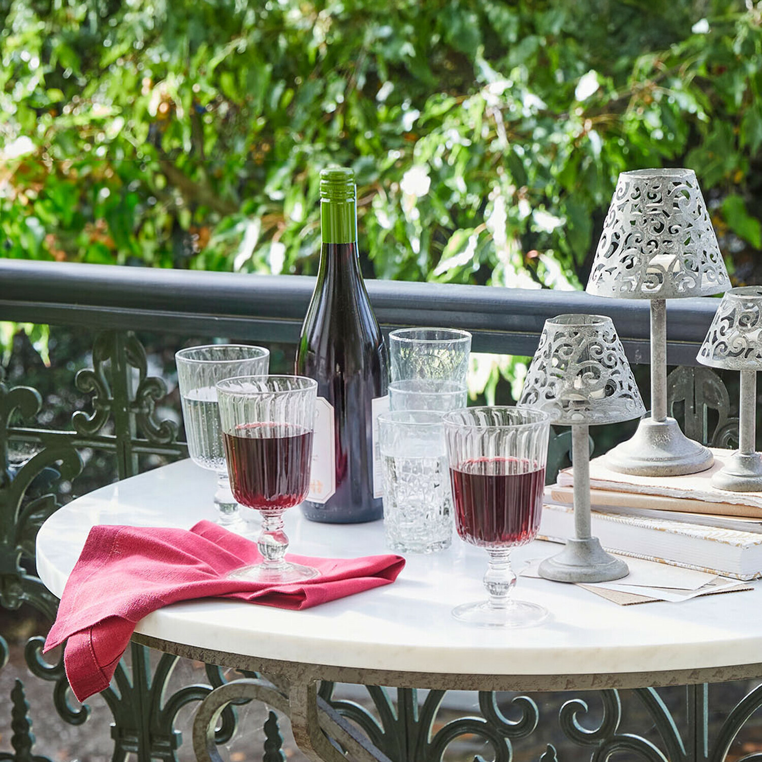 Glazen met rode wijn en fles op witte tafel met decoratieve metalen lampen buiten