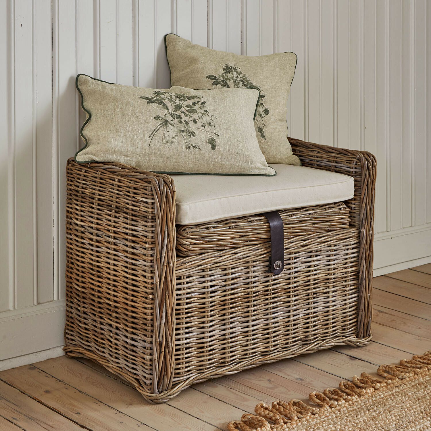 Rotan kist met beige zitkussen en twee decoratieve kussens met plantenmotief voor gezellige ruimtes