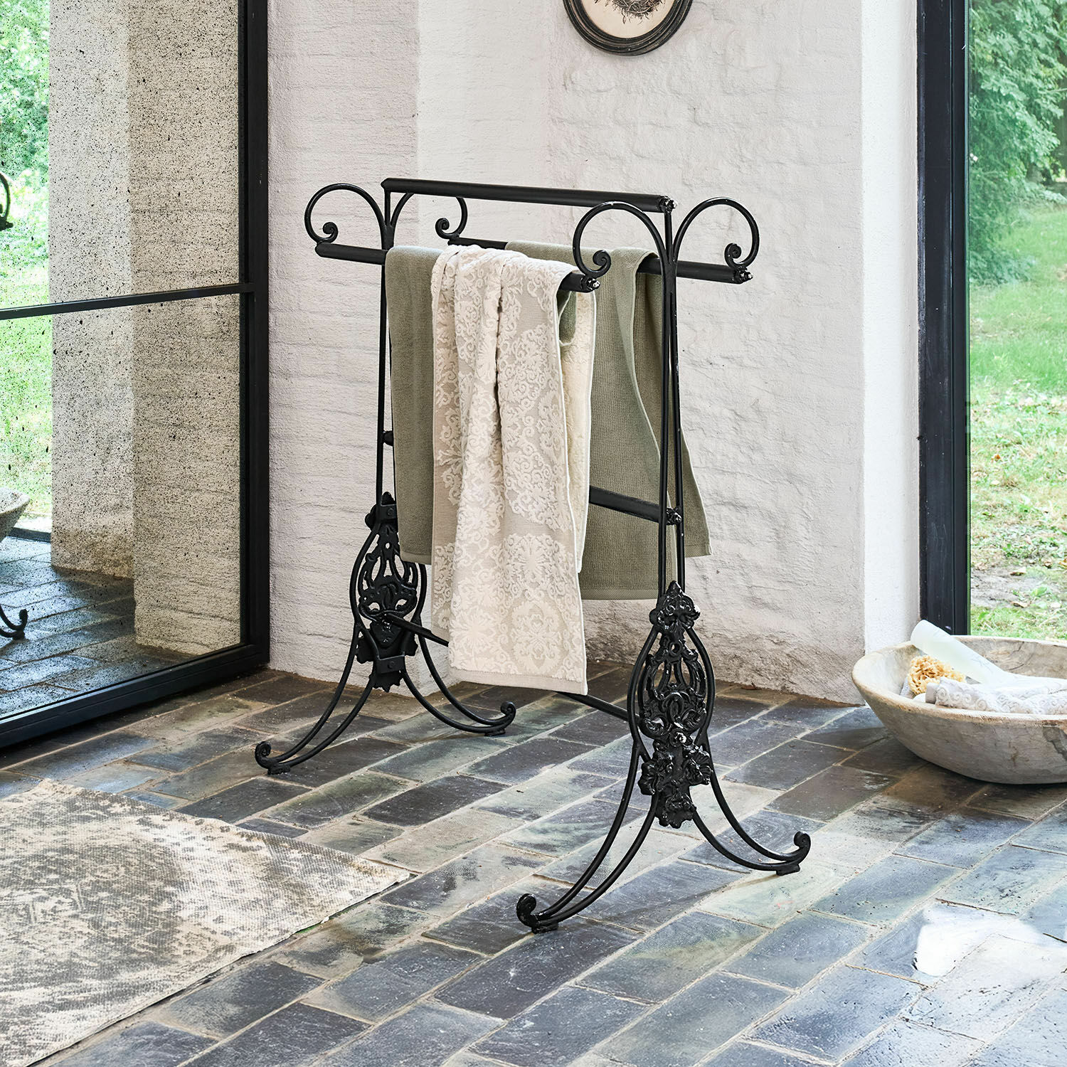 Zwarte metalen handdoekhouder met decoratieve details op stenen vloer in lichte ruimte