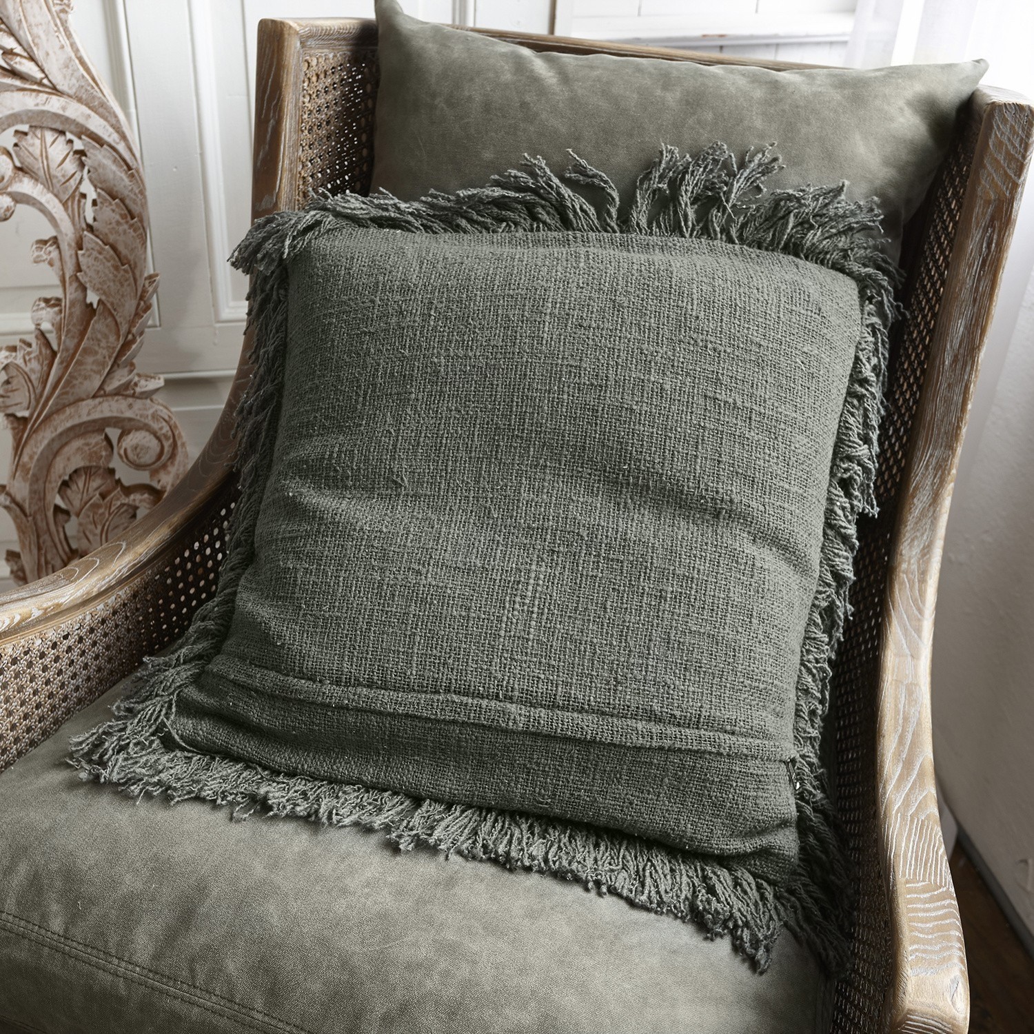 Groen sierkussen met franjes op zachte houten rotanstoel voor interieurdecoratie