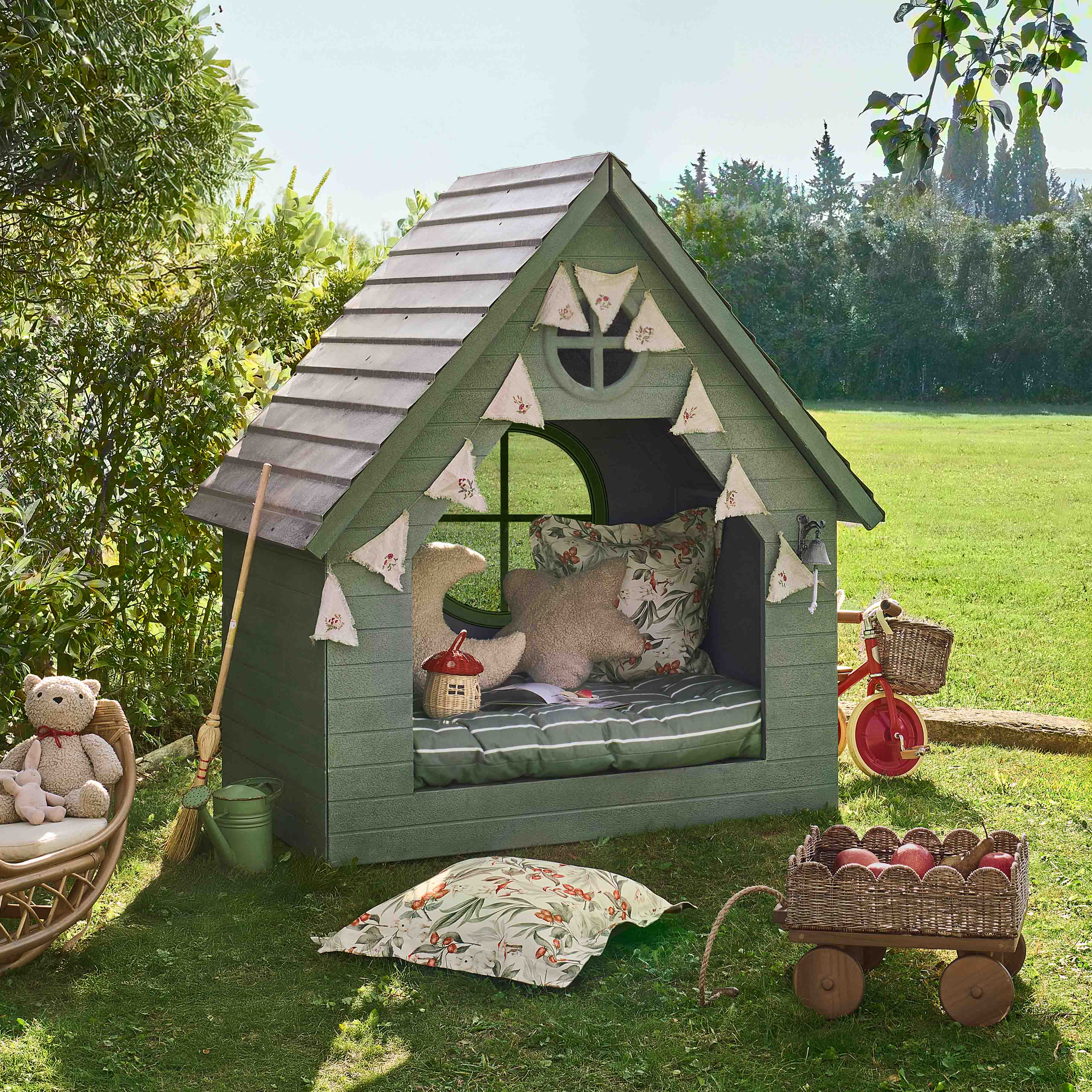 Groen houten tuinhuisje met decoratieve kussens en slinger, perfect voor kinderspel in de tuin.