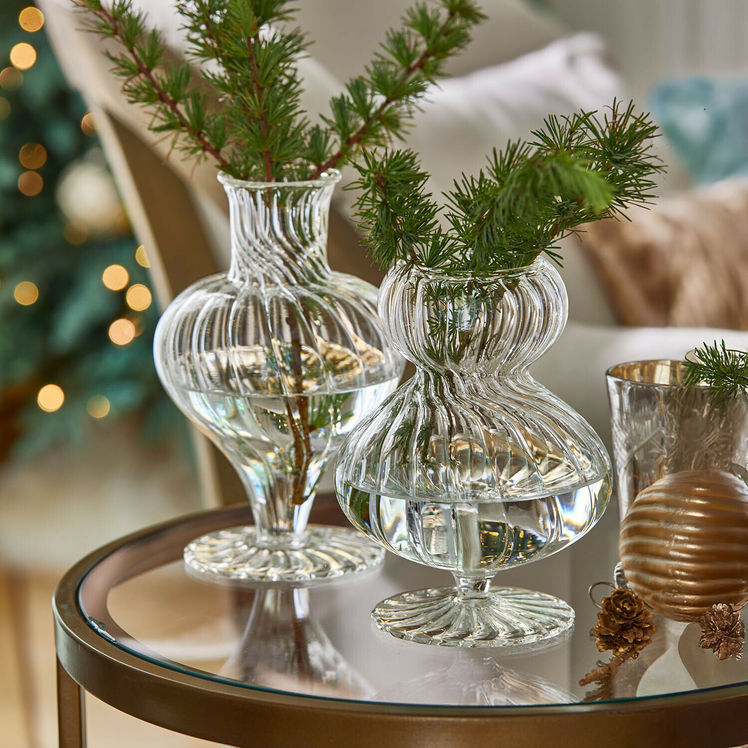 Transparante glazen vazen met groene takken op glazen tafel, feestelijke woondecoratie