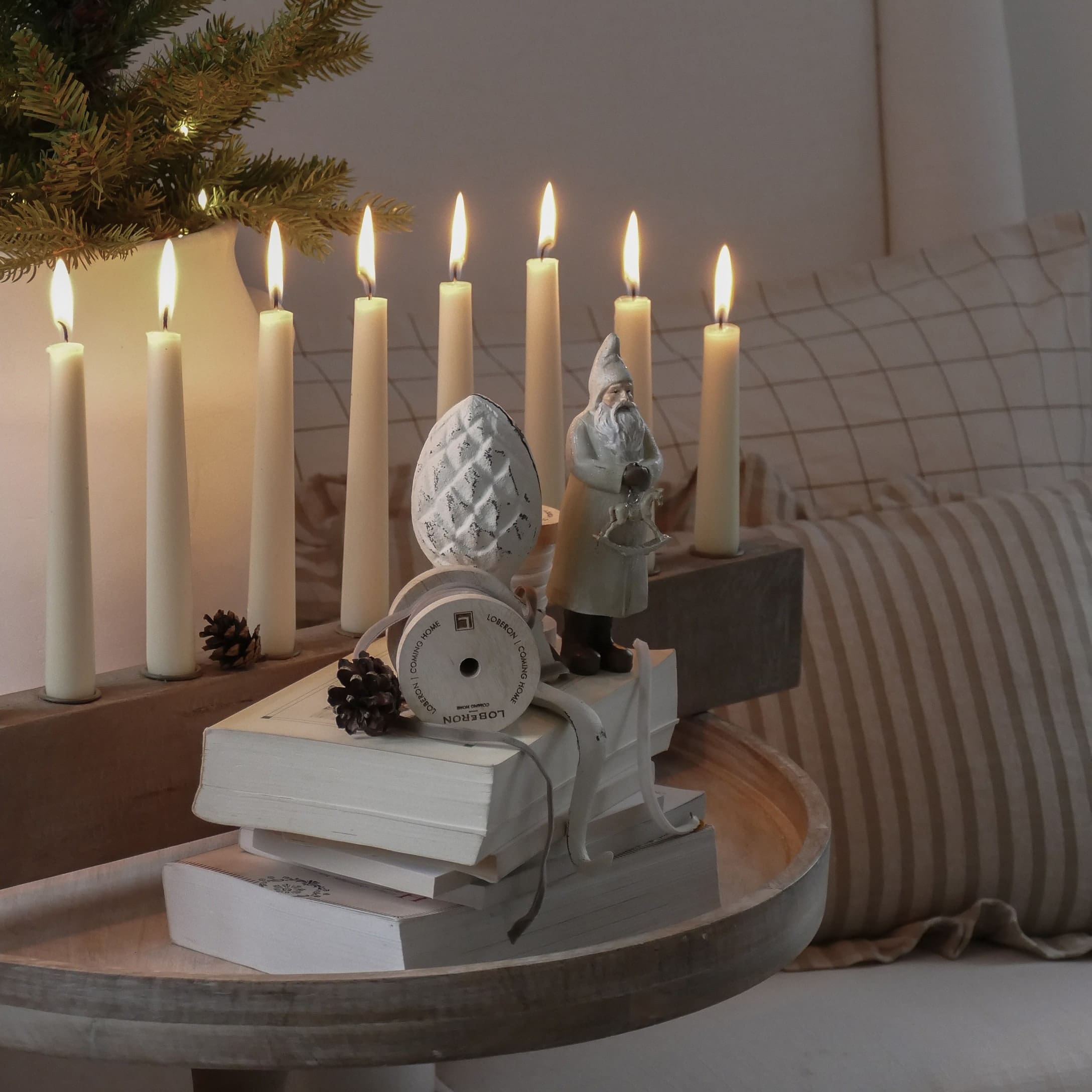 Kerstdecoratie met kerstmanfiguur, brandende kaarsen en boeken op een licht houten dienblad