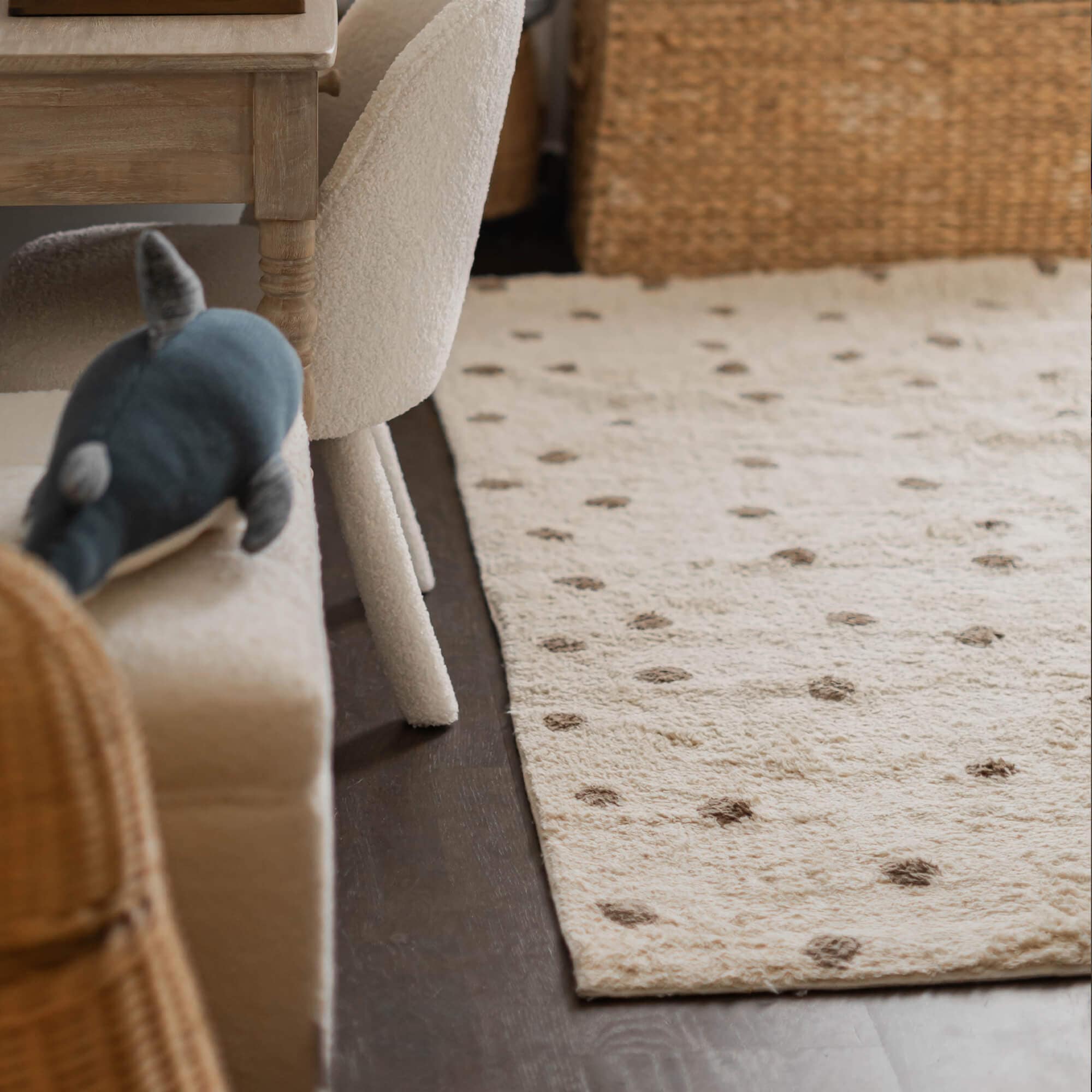 Beige vloerkleed van zacht materiaal met bruine stippen op donkere vloer in woonkamer