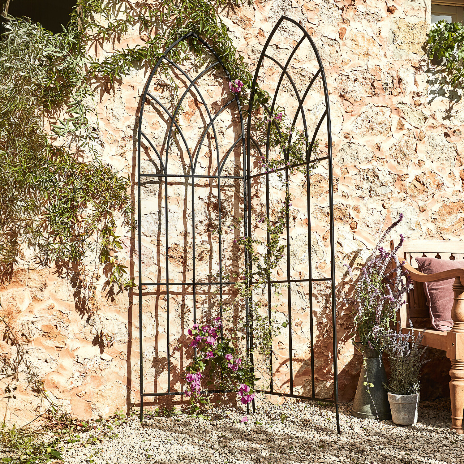 Zwart metalen tuinrank met boogpatroon tegen stenen muur met klimplanten