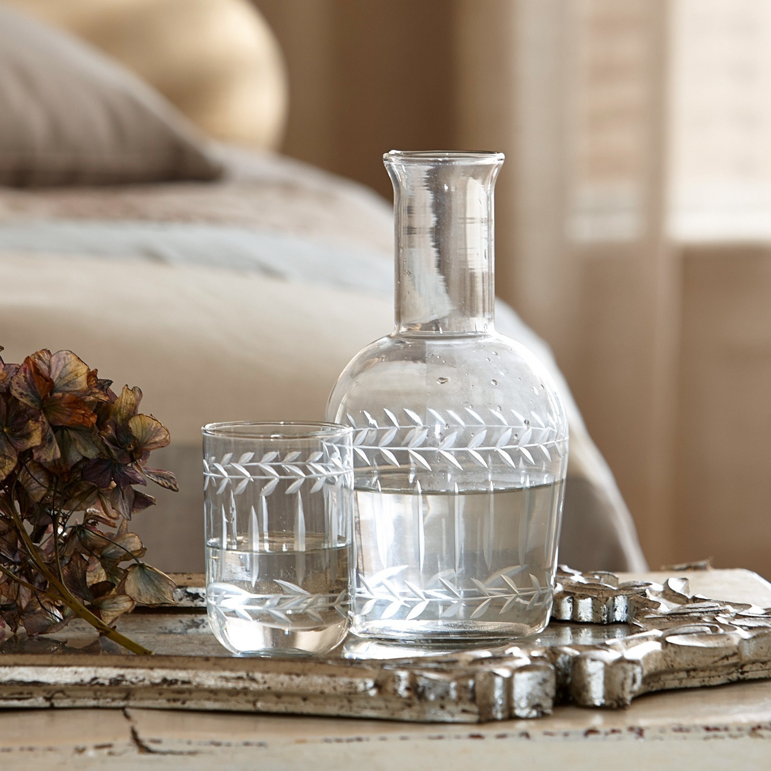 Glazen karaf en glas met gegraveerd bladmotief op beige achtergrond, tafeldecoratie