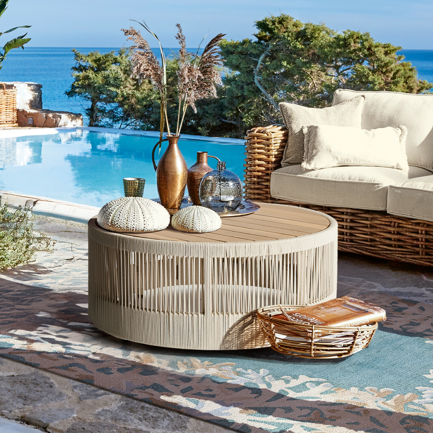 Ronde salontafel van beige touw en hout op terras bij zwembad met decoraties en rotan bank