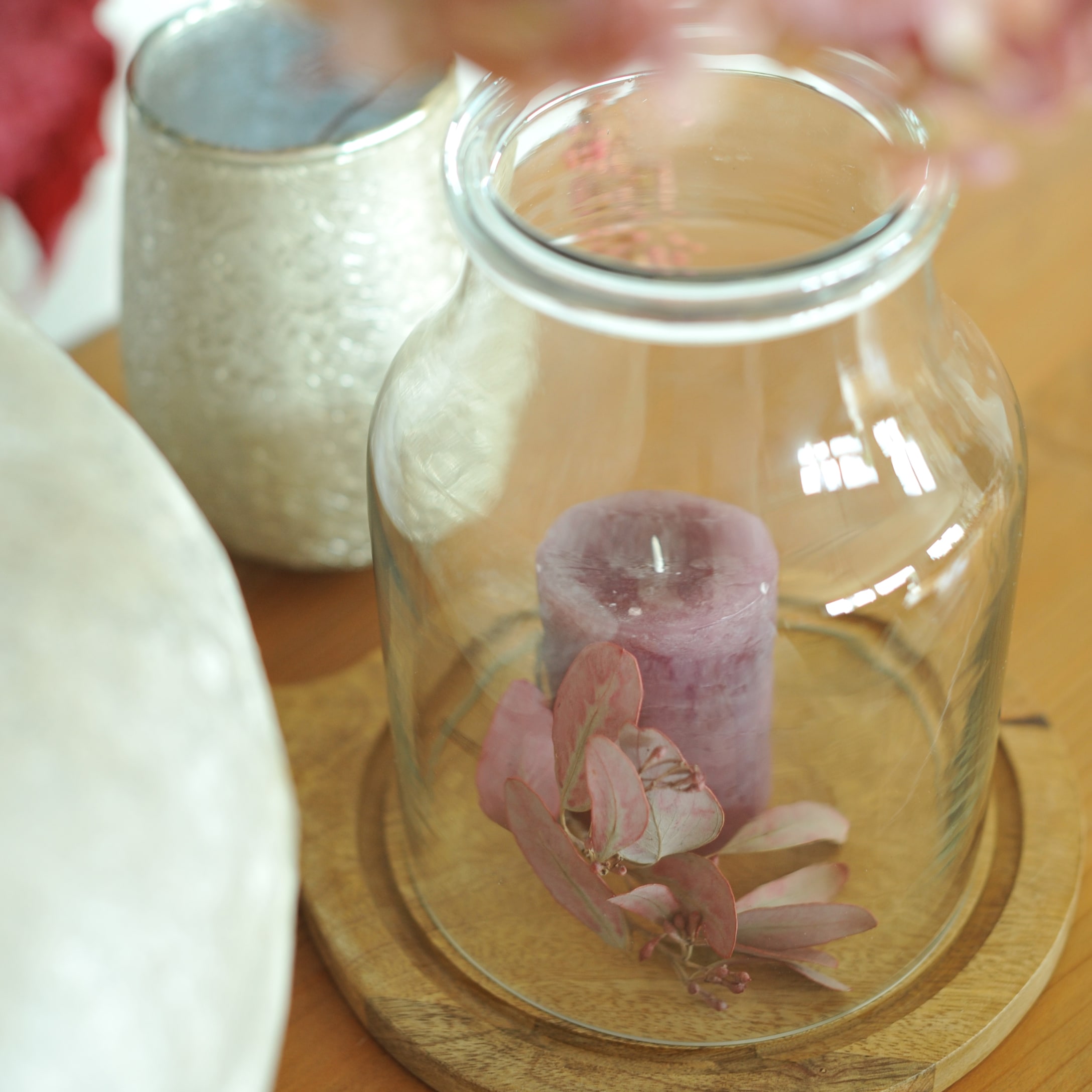 Glazen stolp op houten voet met paarse kaars en roze decoratieve bladeren