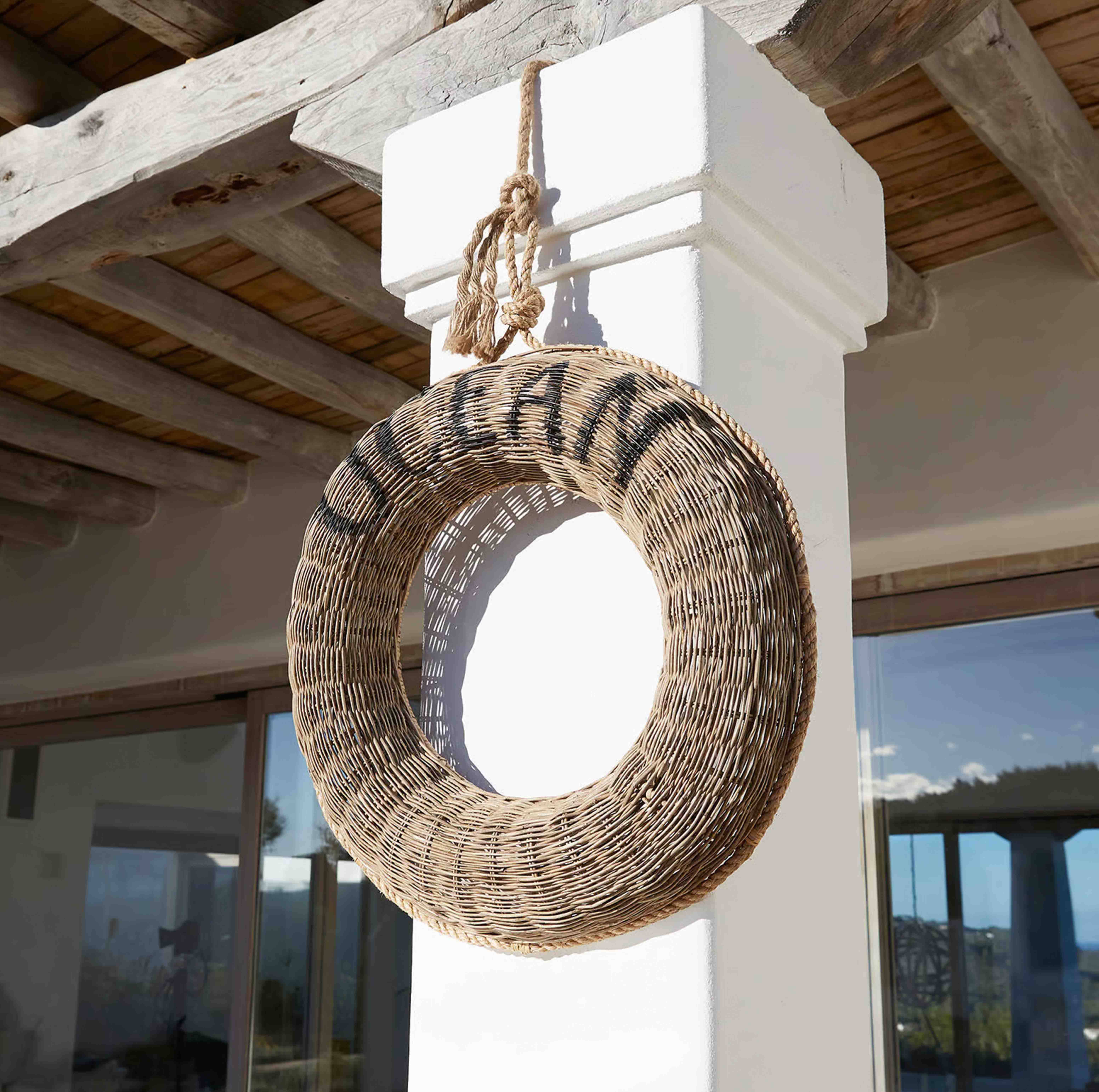 Ronde krans van natuurlijke wilgentenen aan een witte zuil onder een rustiek houten plafond