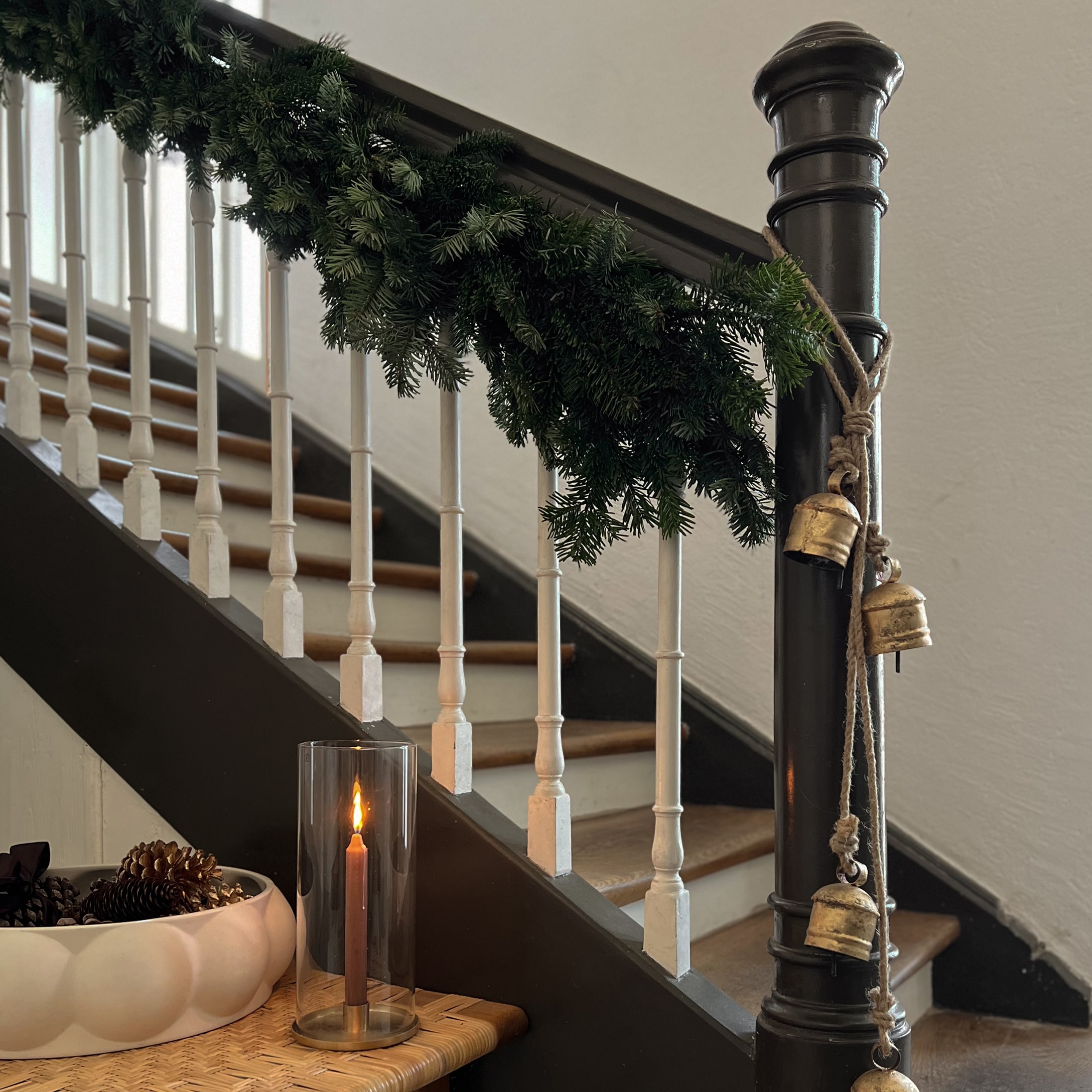 Trapdecoratie met groene dennenguirlande, gouden belletjes en brandende kaars in glazen windlicht